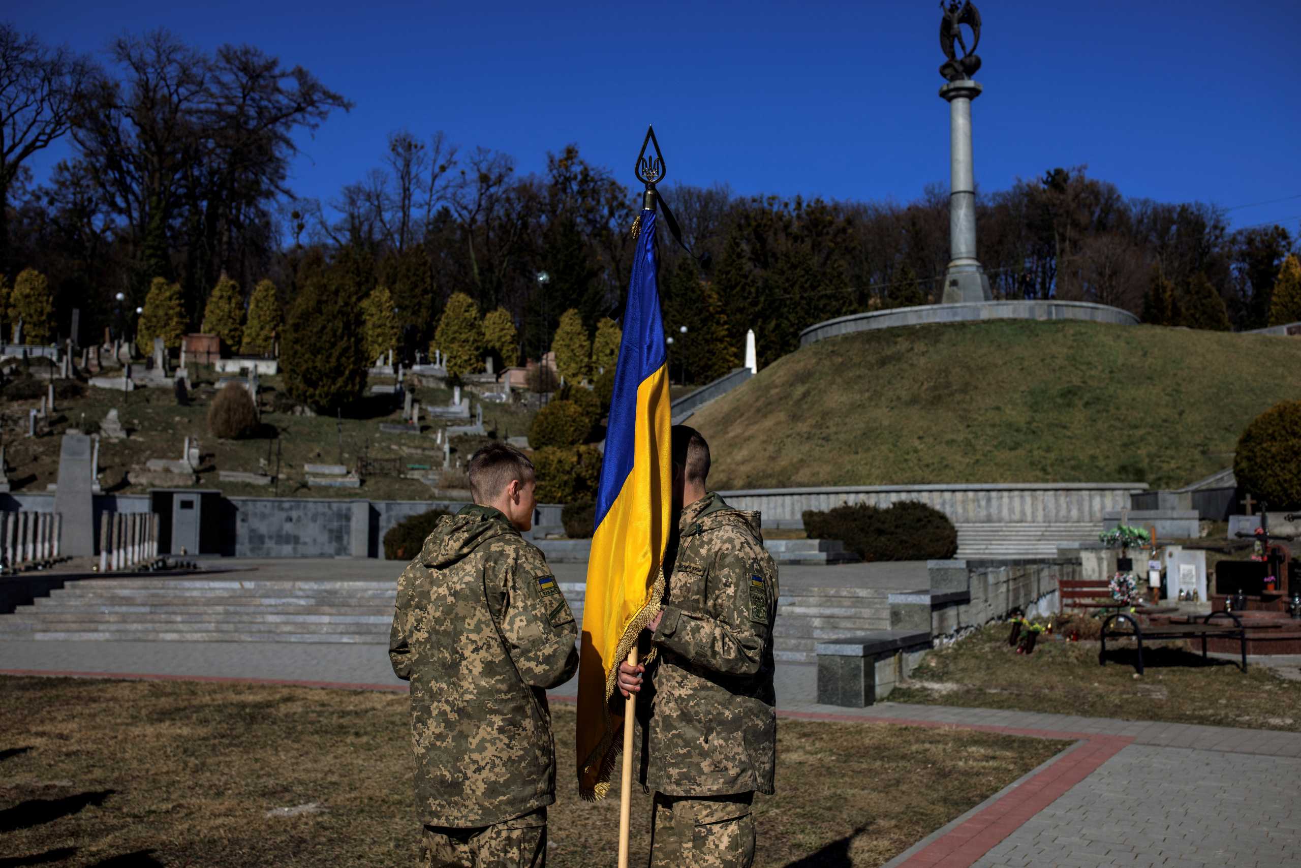 A soldier holds a Ukrainian national flag as he talks to a fellow soldier during the funeral of sergeant Kostiantyn Deriuhin, 44, who was killed in battle during Russia's attack on Ukraine, at the Lychakiv cemetery in Lviv, Ukraine, March 27, 2022. REUTERS
