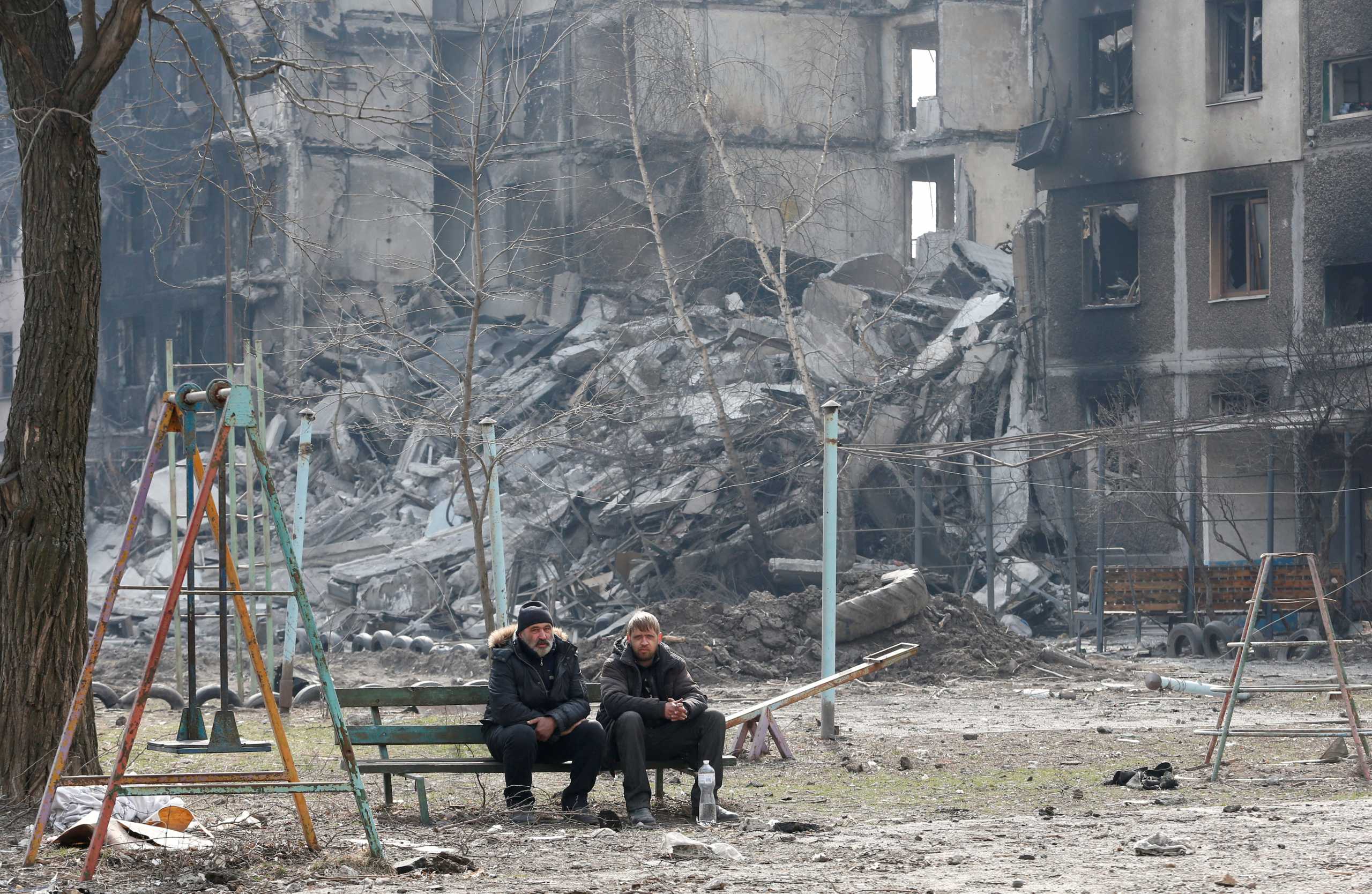 Local residents sit on a bench near an apartment building destroyed in the course of Ukraine-Russia conflict in the besieged southern port city of Mariupol, Ukraine March 25, 2022. REUTERS