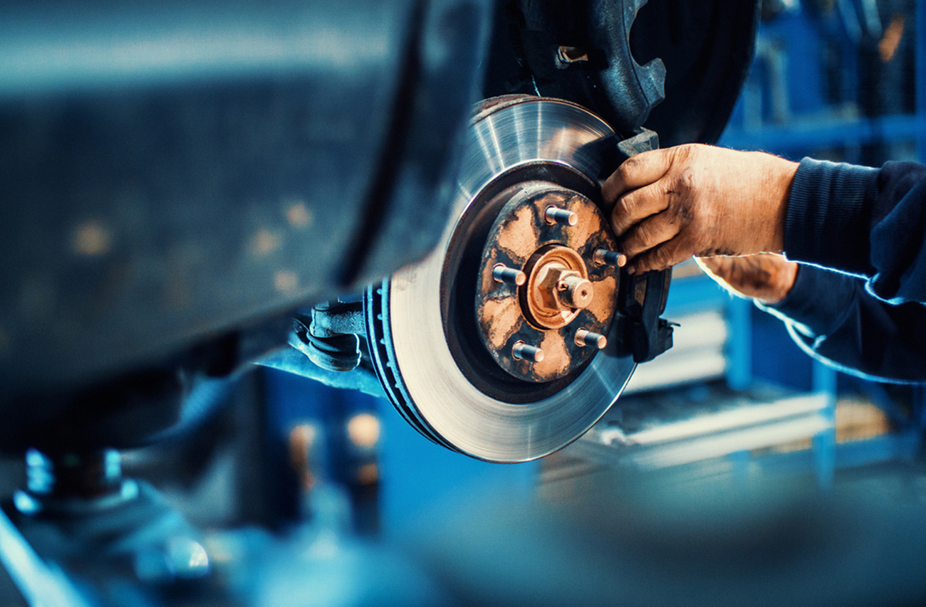 Closeup of unrecognizable mechanic replacing car brake pads. The car is lifted with hydraulic jack at eye level.
