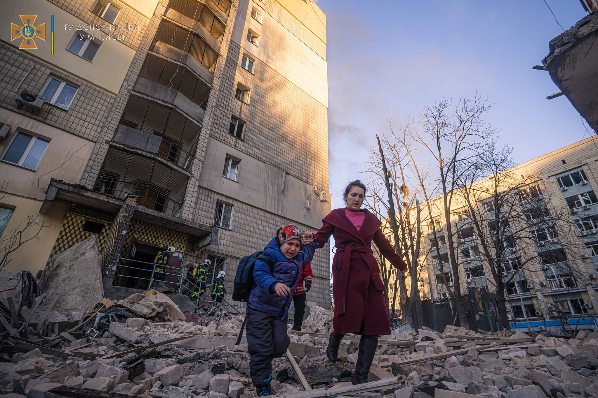 A woman with a child evacuates from a residential building damaged by shelling, as Russia's attack on Ukraine continues, in Kyiv, Ukraine, in this handout picture released March 16, 2022.  Press service of the State Emergency Service of Ukraine