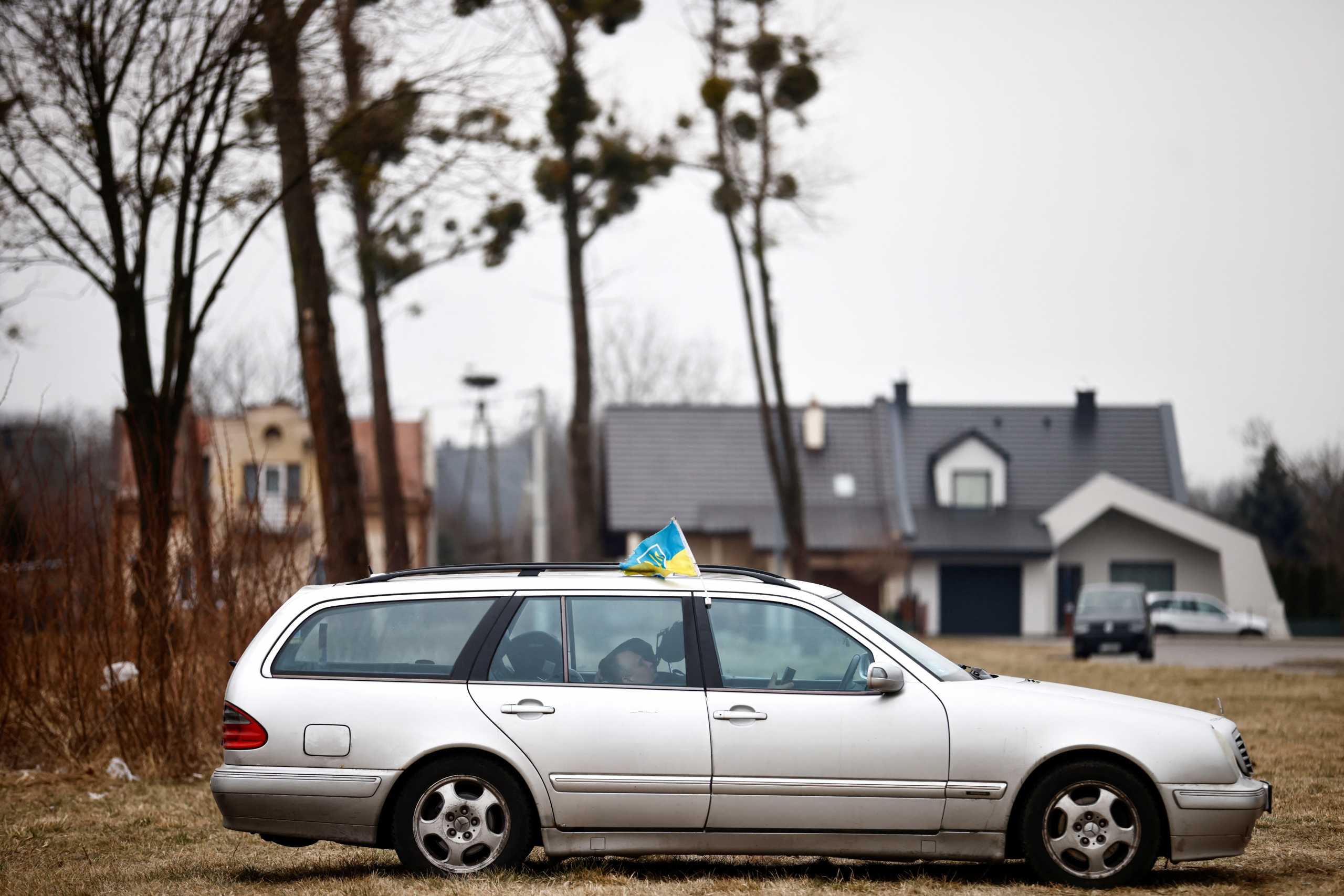 A man rests in a car with a Ukrainian flag hanging from the window, as refugees who fled the Russian invasion of Ukraine gather at a temporary camp in Przemysl, Poland, March 2, 2022. REUTERS