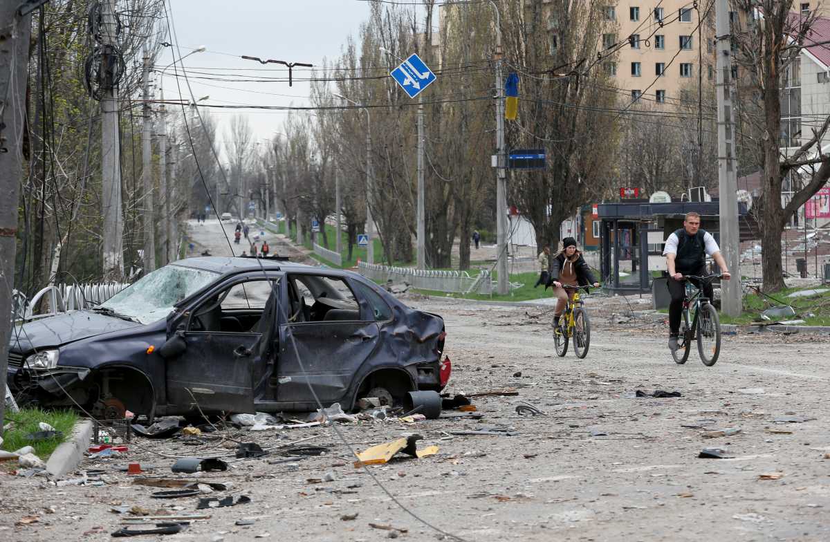 People ride bicycles near a car destroyed during Ukraine-Russia conflict in the southern port city of Mariupol, Ukraine April 18, 2022. REUTERS