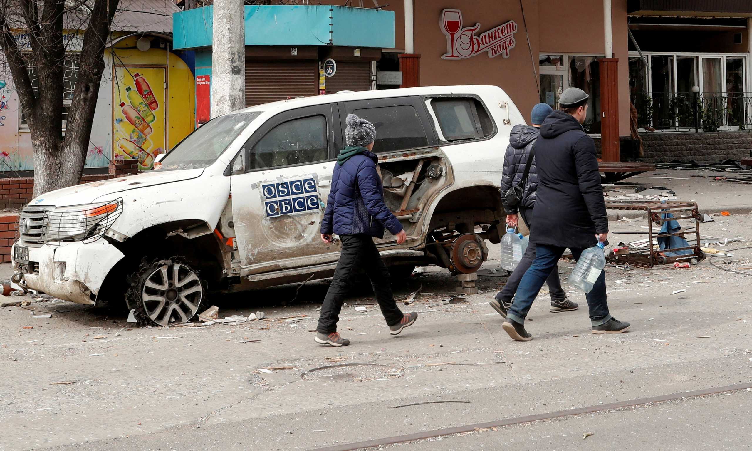 FILE PHOTO: People walk past an OSCE car damaged in the course of Ukraine-Russia conflict in the southern port city of Mariupol, Ukraine April 1, 2022. REUTERS
