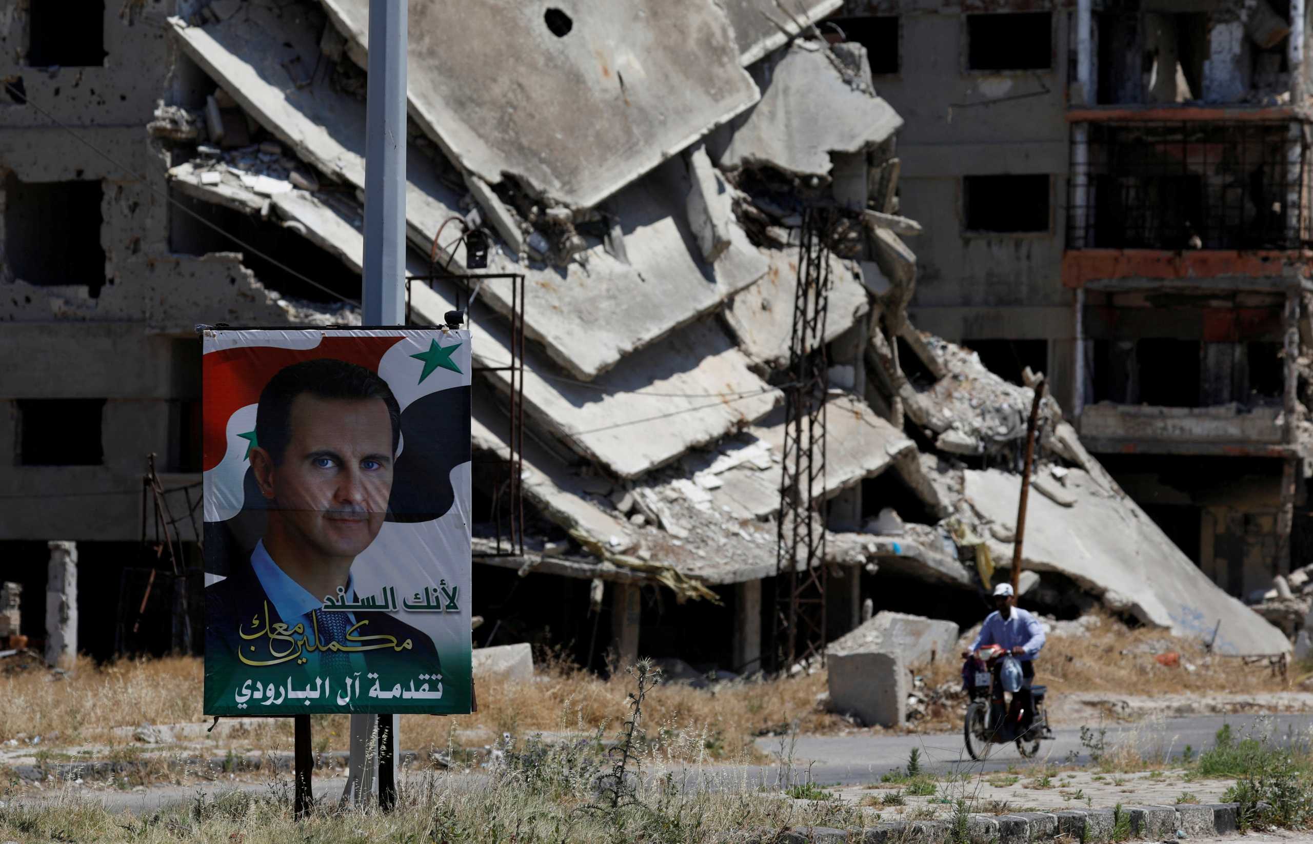 FILE PHOTO: A poster depciting Syria's President Bashar al-Assad is pictured in front of damaged buildings, ahead of the May 26 presidential election, in Homs, Syria May 23, 2021.  Picture taken May 23, 2021. REUTERS