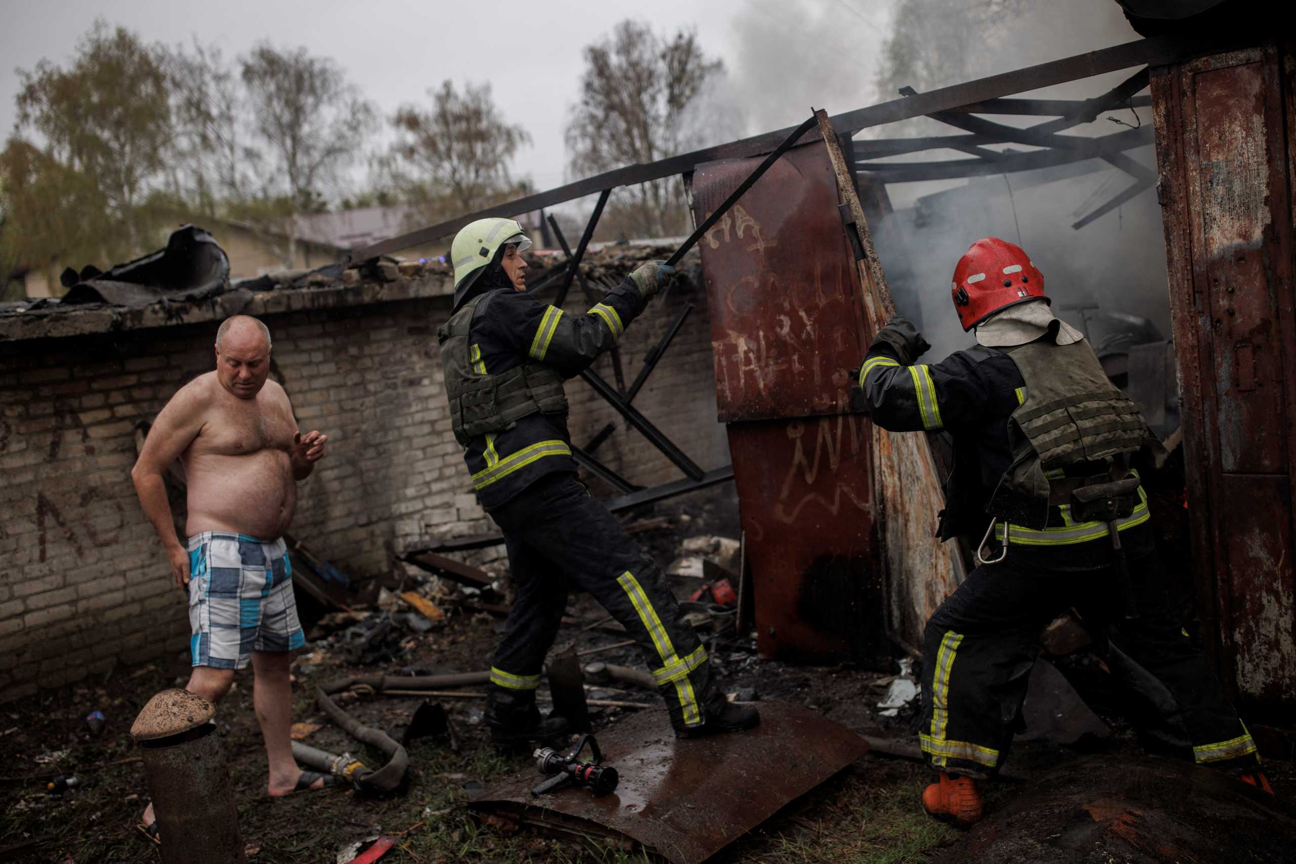 Local Volodymir, 45, stands next to firefighters who try to extinguish a fire burning at his garage, following Russian shelling, amid Russia's attack on Ukraine, in Kharkiv, Ukraine, April 18, 2022. REUTERS