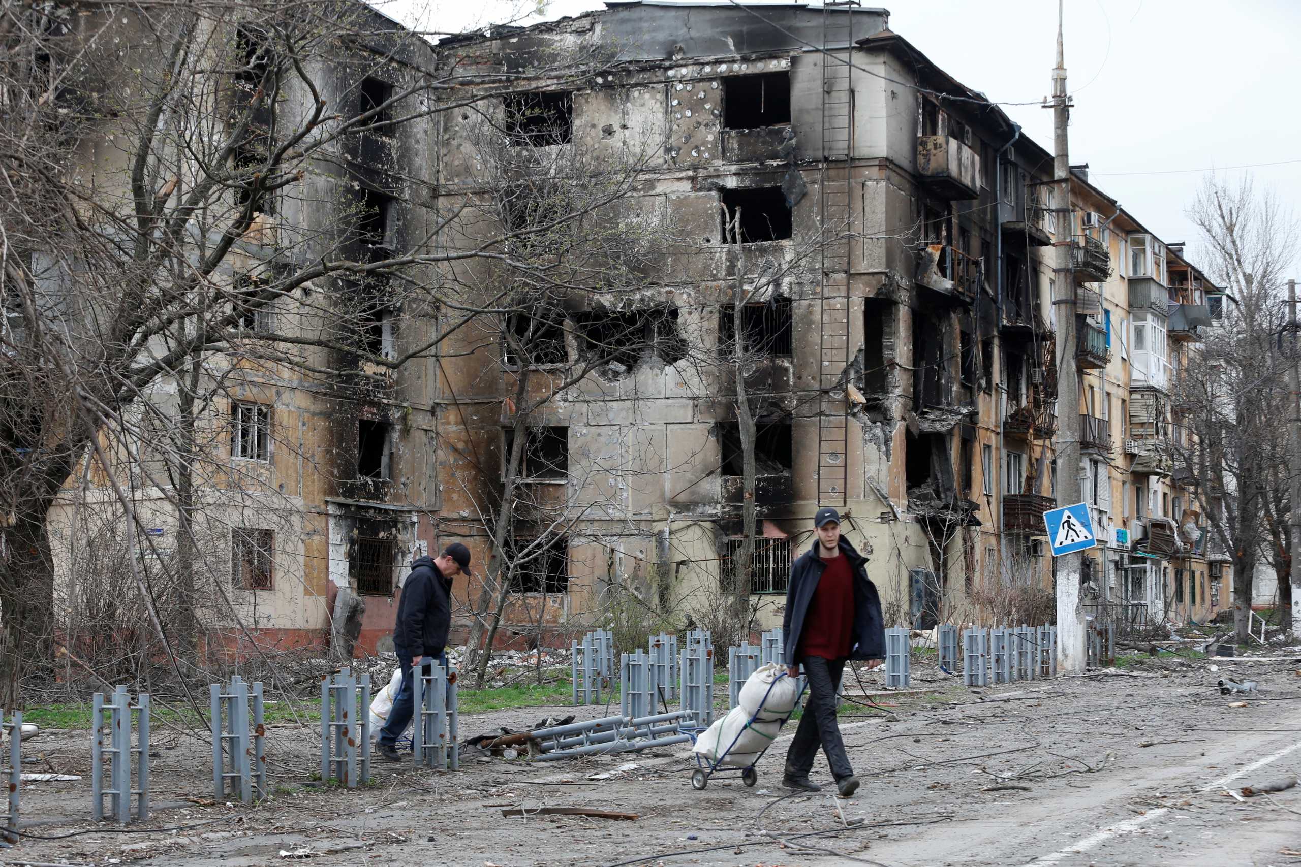 People walk past a residential building, which was heavily damaged during Ukraine-Russia conflict in the southern port city of Mariupol, Ukraine April 18, 2022. REUTERS