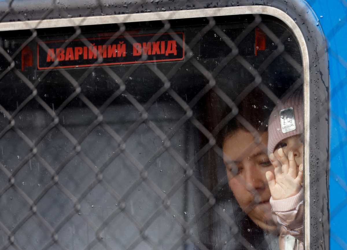 A Ukrainian refugee child looks out through a window labelled 'emergency exit' in Ukrainian, on a train from Odesa, after fleeing Russia's invasion of Ukraine, at Przemysl Glowny train station in Przemysl, Poland, April 9, 2022.    REUTERS
