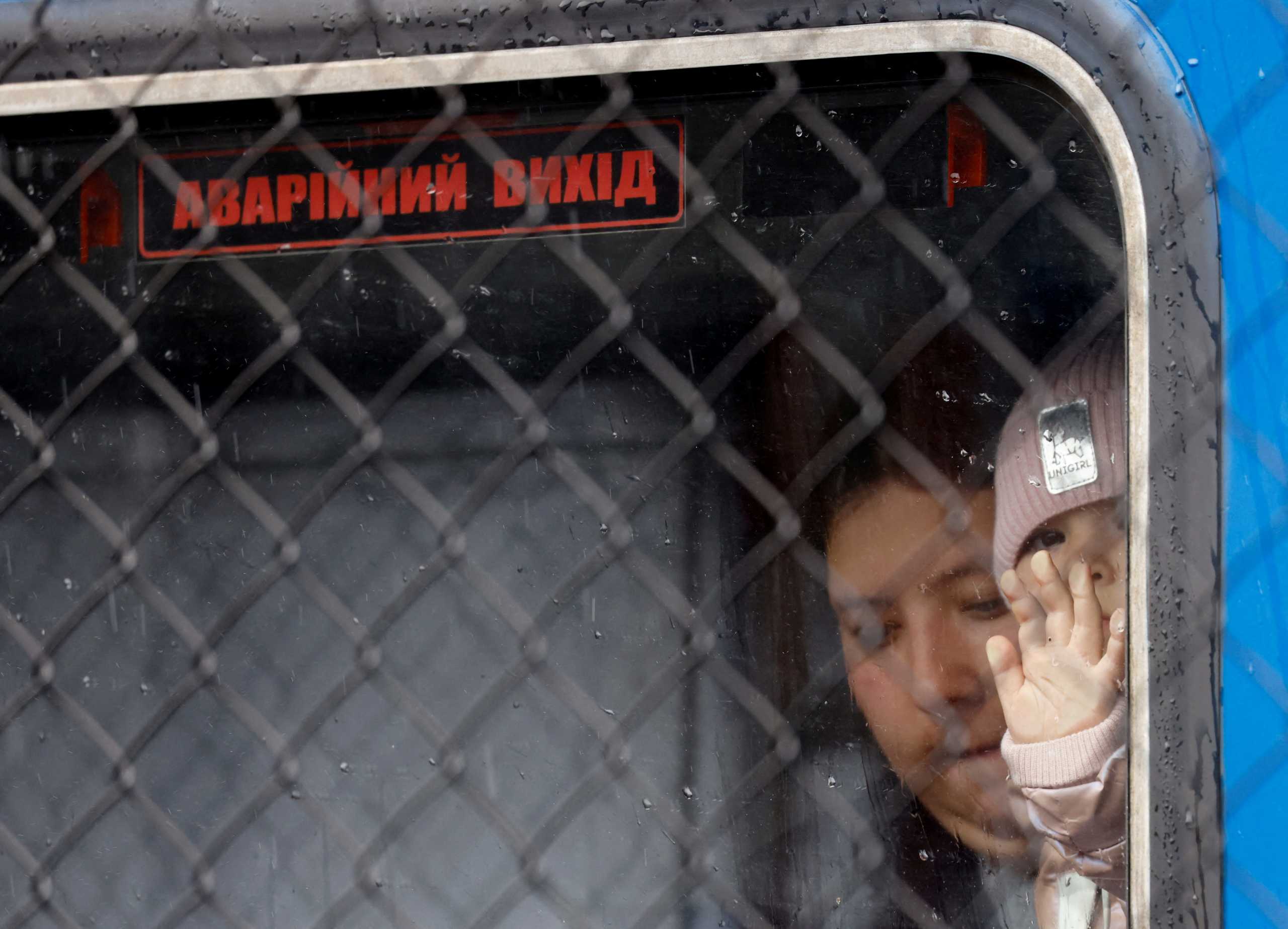 A Ukrainian refugee child looks out through a window labelled 'emergency exit' in Ukrainian, on a train from Odesa, after fleeing Russia's invasion of Ukraine, at Przemysl Glowny train station in Przemysl, Poland, April 9, 2022.    REUTERS