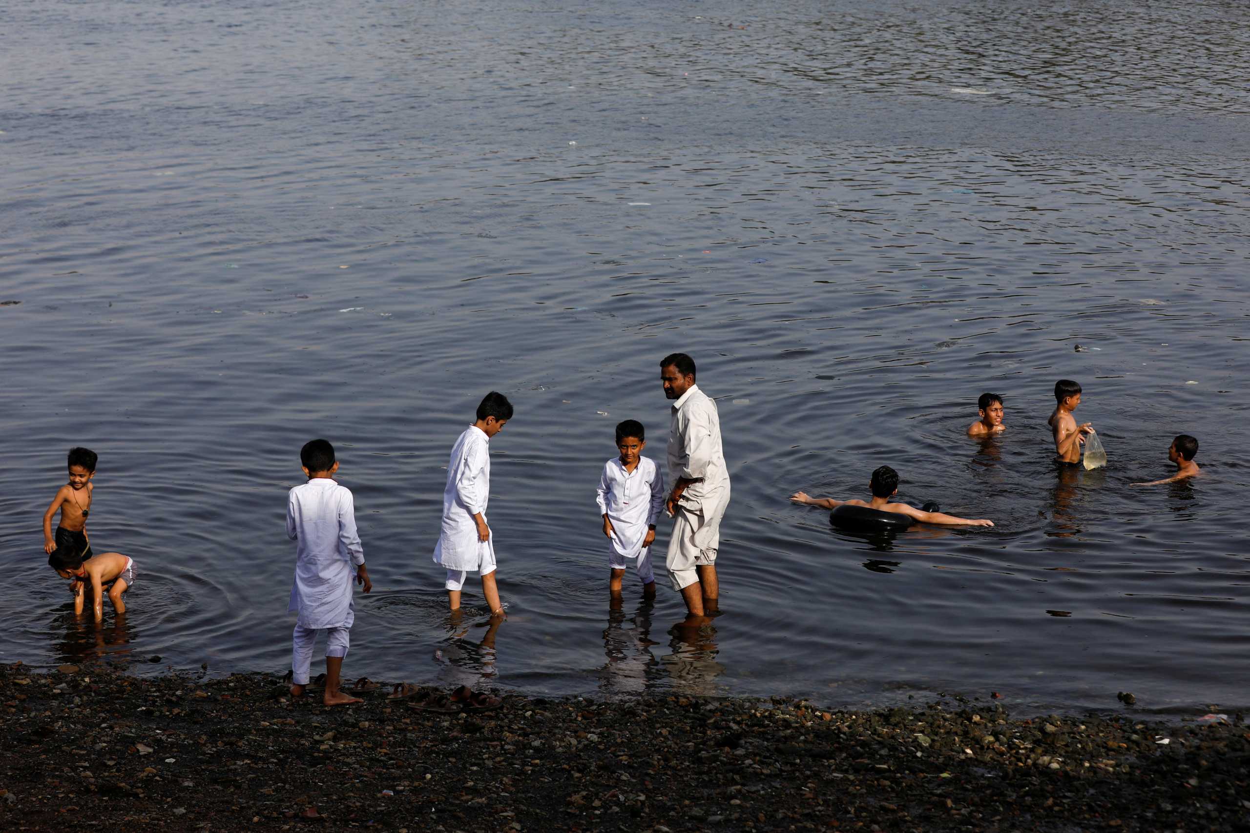 A man and children cool off during hot and humid day at China Creek area in Karachi, Pakistan, April 29, 2022. REUTERS
