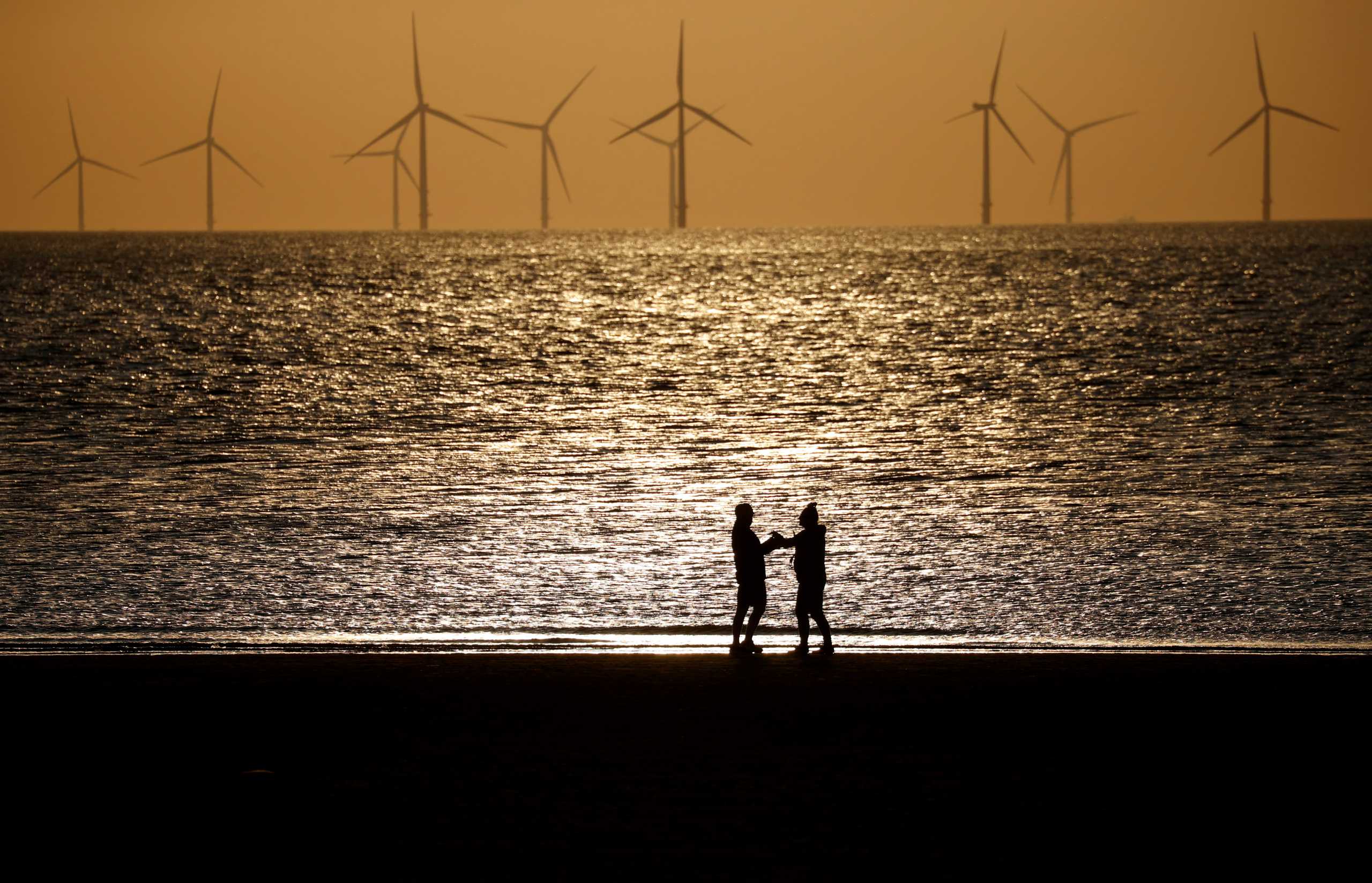 People walking at New Brighton beach with the Burbo Bank windfarm behind before sunset, following the outbreak of the coronavirus disease (COVID-19), New Brighton, Britain, May 5, 2020. REUTERS