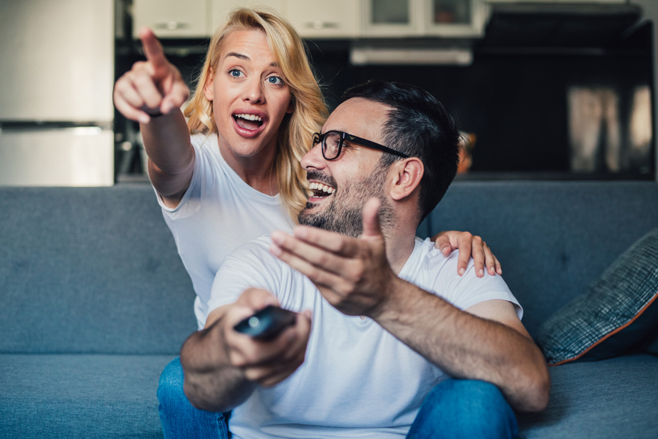 Beautiful young happy couple sitting on a couch at home and watching tv.