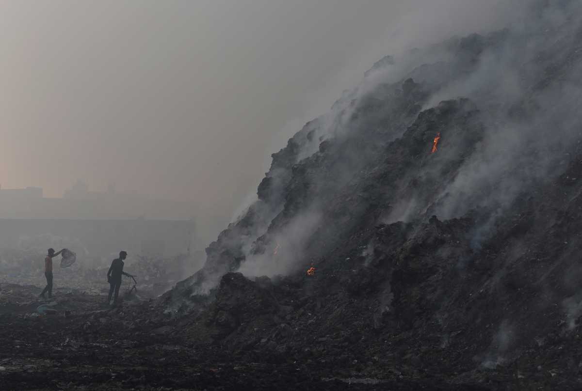 Waste collectors look for recyclable materials as smoke billows from burning garbage at the Bhalswa landfill site in New Delhi, India, April 27, 2022. REUTERS