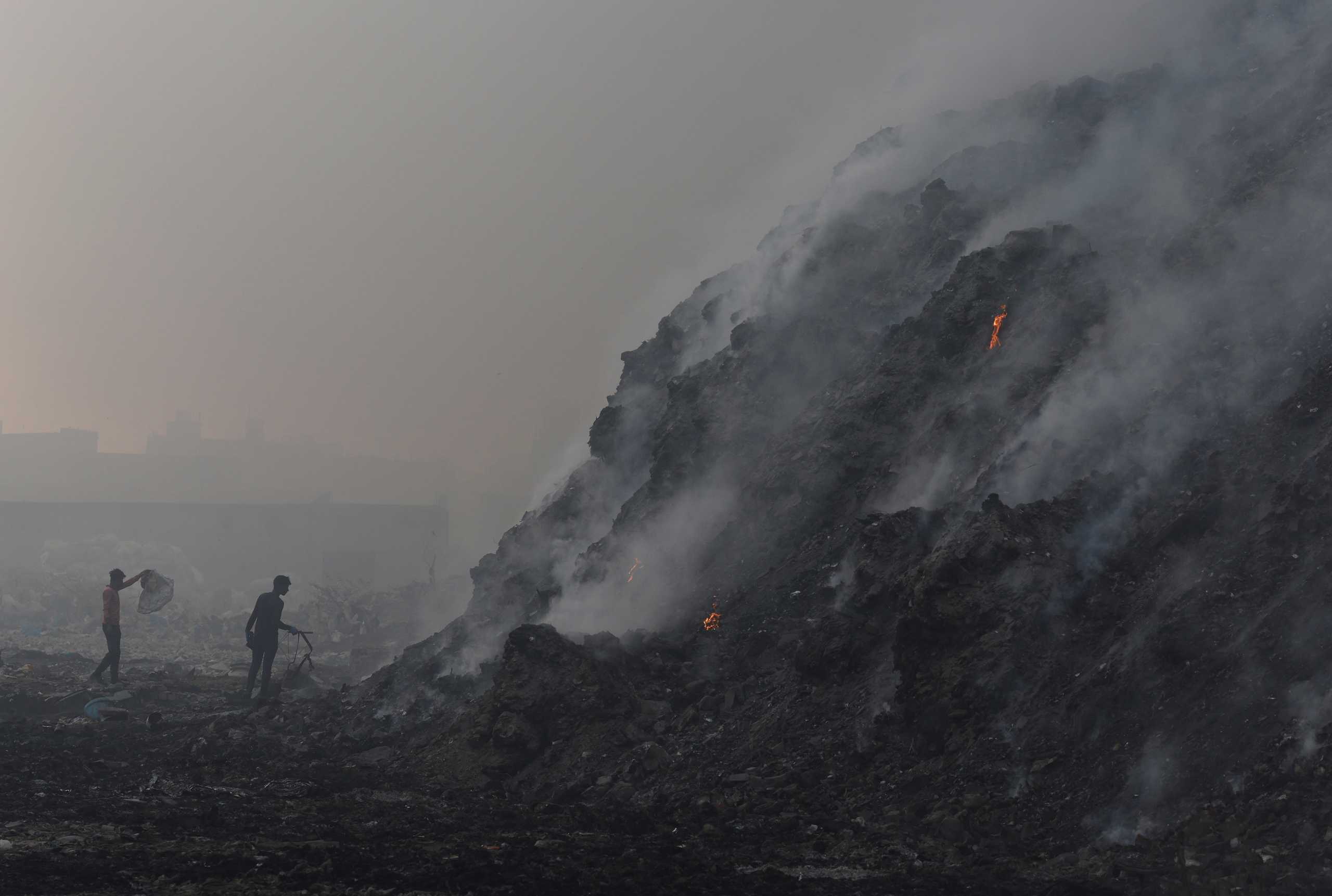 Waste collectors look for recyclable materials as smoke billows from burning garbage at the Bhalswa landfill site in New Delhi, India, April 27, 2022. REUTERS
