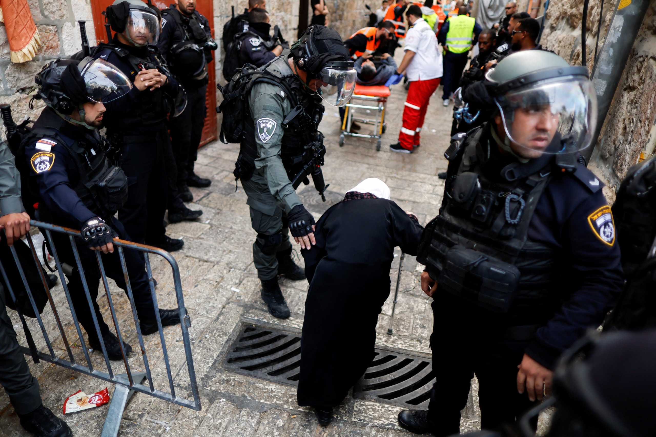 An Israeli border police officer assists an elderly Palestinian woman at a temporary street block while an injured Palestinian man is evacuated in Jerusalem's Old City April 17, 2022. REUTERS