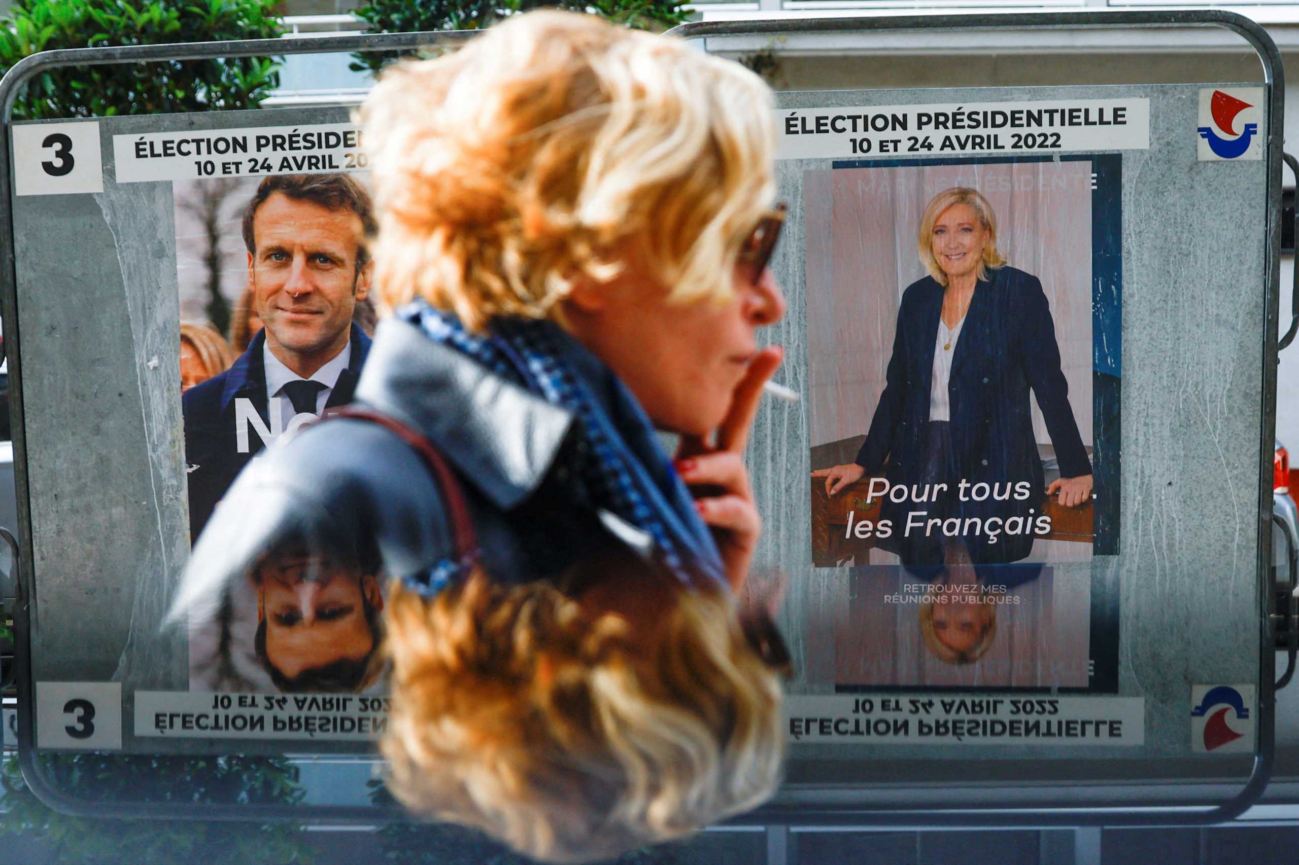 A woman walks past official campaign posters of French presidential election candidates Marine le Pen, leader of French far-right National Rally (Rassemblement National) party, and French President Emmanuel Macron, candidate for his re-election, displayed on an official billboard in Paris, France, April 19, 2022. REUTERS