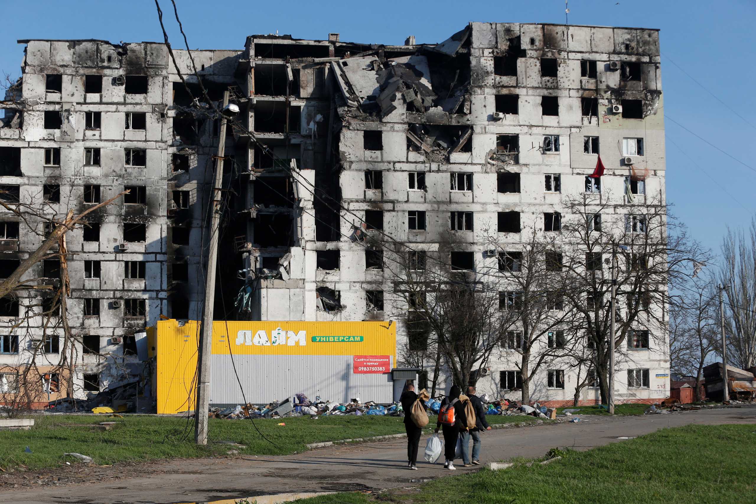 Local residents walk past an apartment building destroyed during Ukraine-Russia conflict in the southern port city of Mariupol, Ukraine April 20, 2022. REUTERS