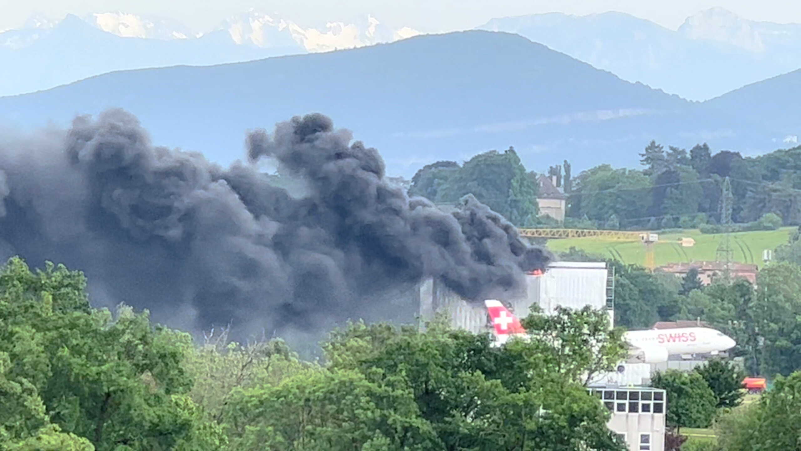 A plane flies past as smoke rises after a fire broke out near Geneva airport in Switzerland May 20, 2022 in this screen grab obtained from a video on social media and taken from Ferney-Voltaire, France. Alexandra La Guardia