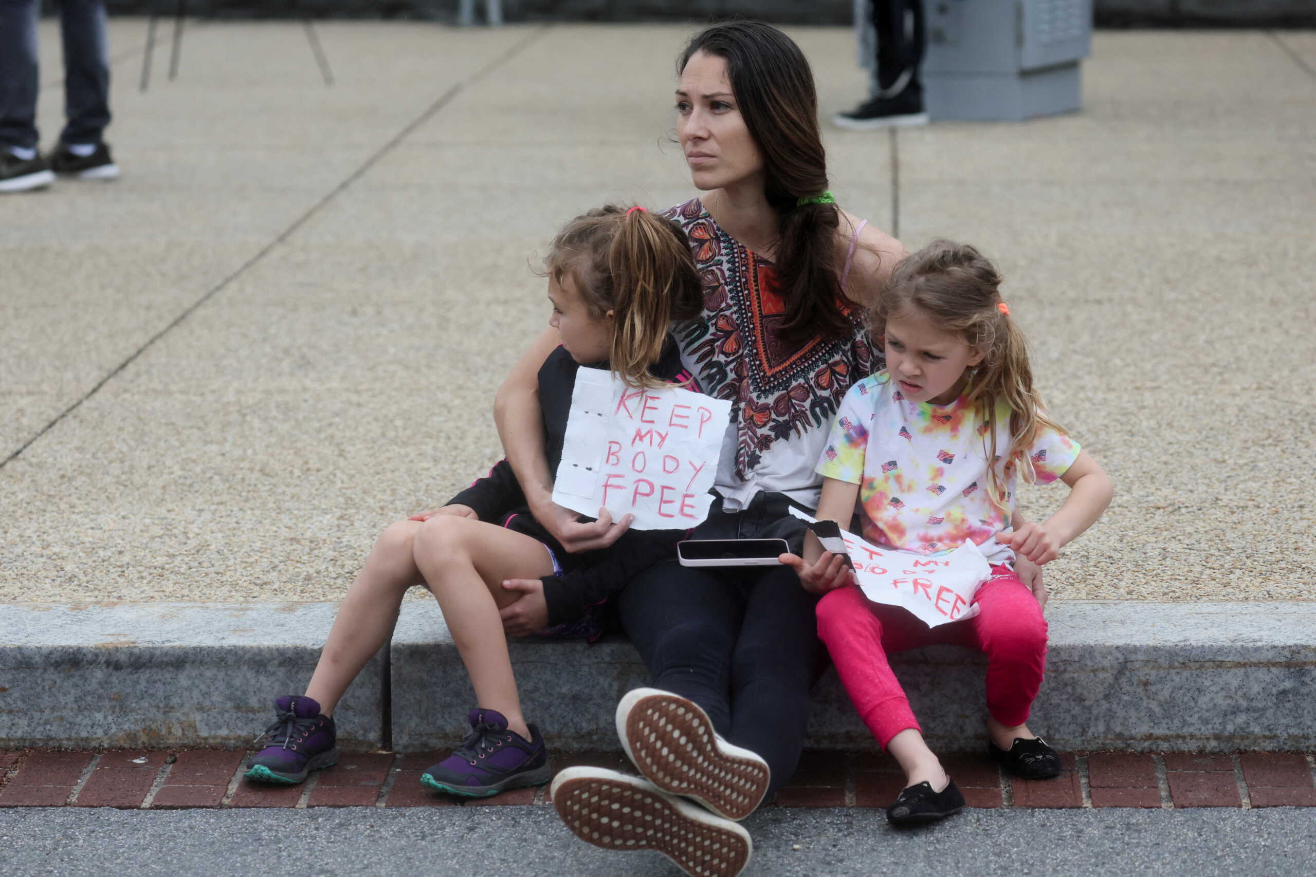Abortion rights protester Maggy Benson sits on the sidewalk with her daughters as she participates in nationwide demonstrations following the leaked Supreme Court opinion suggesting the possibility of overturning the Roe v. Wade abortion rights decision, in Washington, U.S., May 14, 2022. REUTERS
