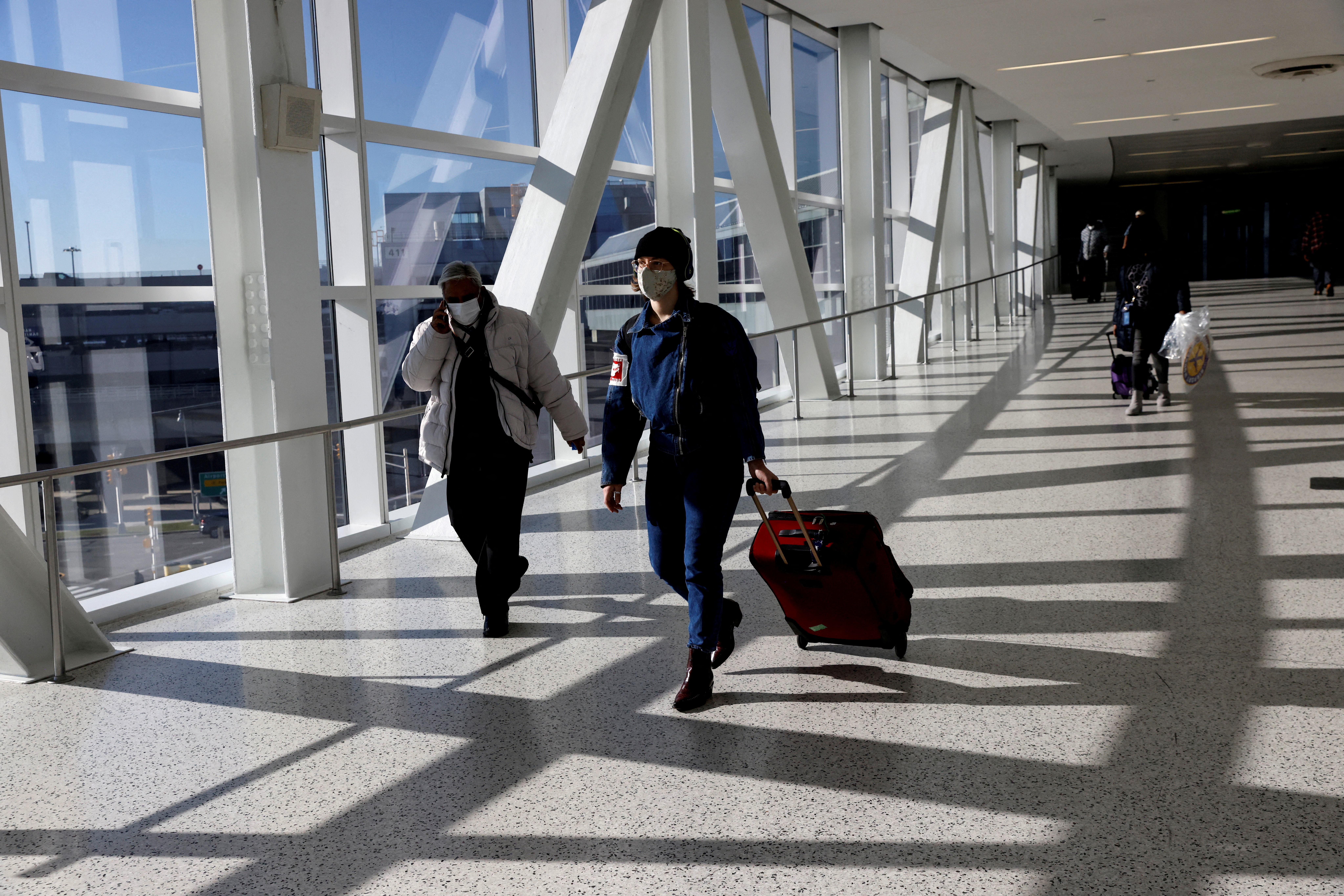 FILE PHOTO: Air travellers wearing protective face masks, amid the coronavirus disease (COVID-19) pandemic, walk at JetBlue Terminal 5 at JFK International airport in New York, U.S., November 16, 2021. REUTERS