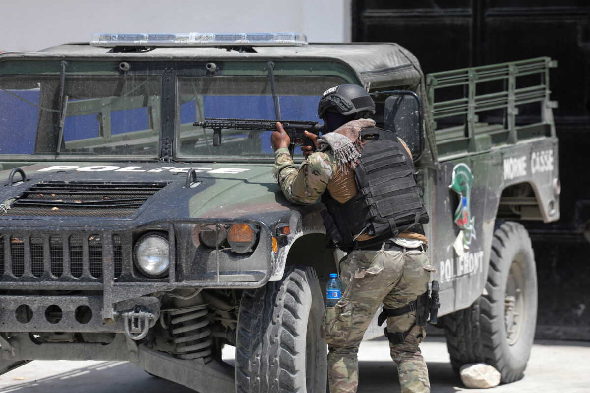 A member of the Haitian National Police takes cover behind a police vehicle while patrolling as ongoing gun battles between rival gangs have forced residents to flee their homes, in Port-Au-Prince, Haiti April 28, 2022. REUTERS