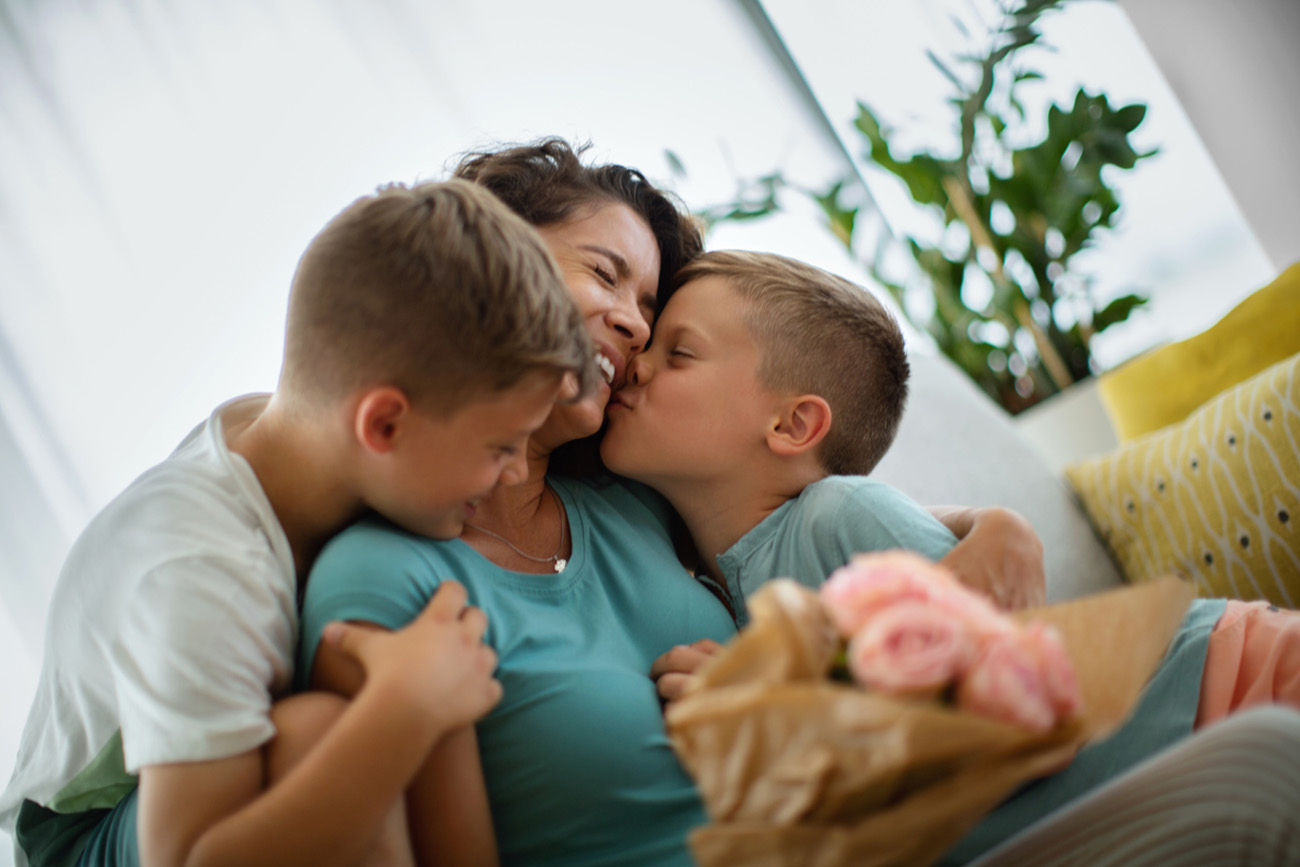 Sons hugging and kissing their mother and giving her a bouquet of roses for Mother's Day.