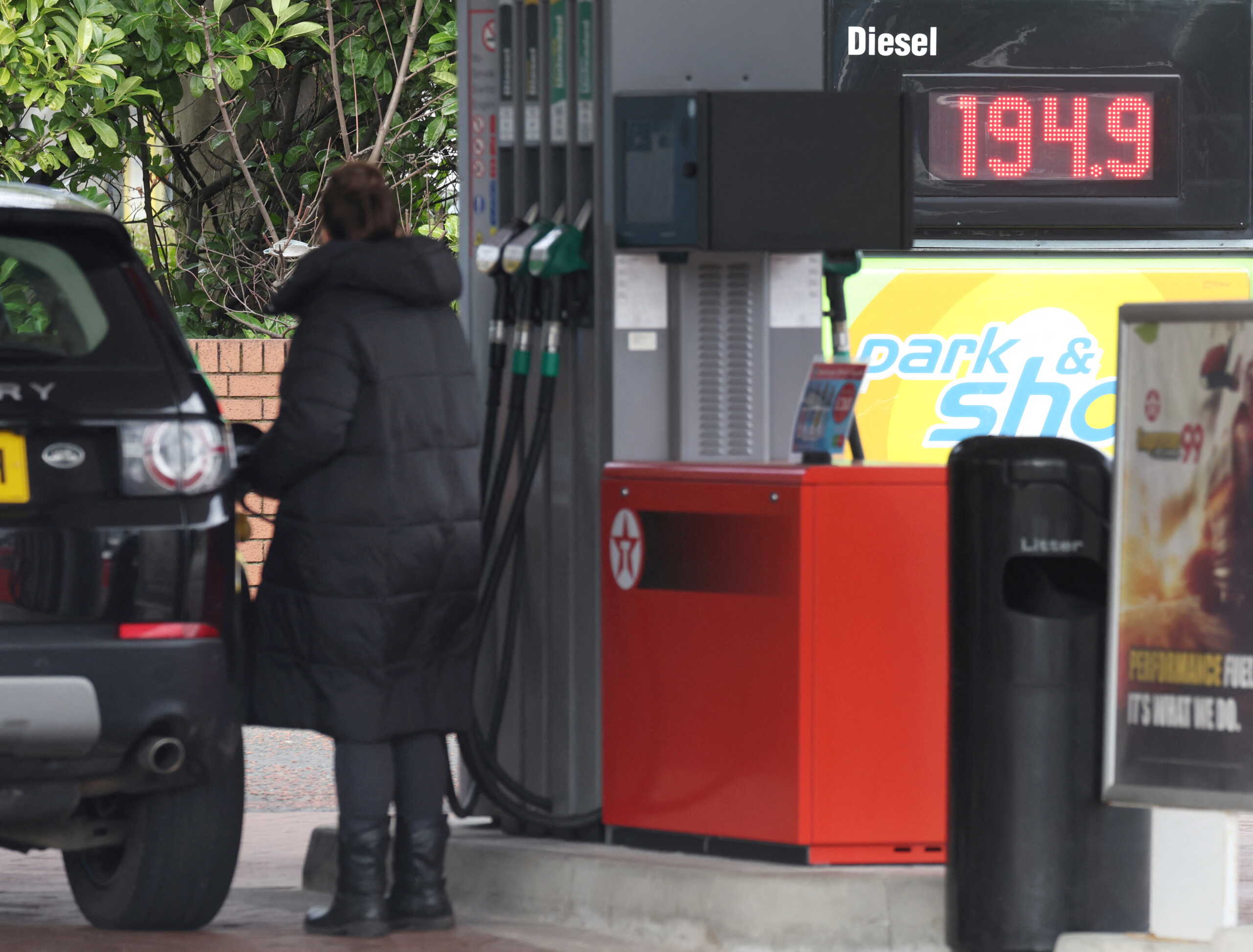 FILE PHOTO: A woman fills up her car in front of a sign showing increased fuel prices at a filling station near Liverpool, Britain, March 10, 2022. REUTERS
