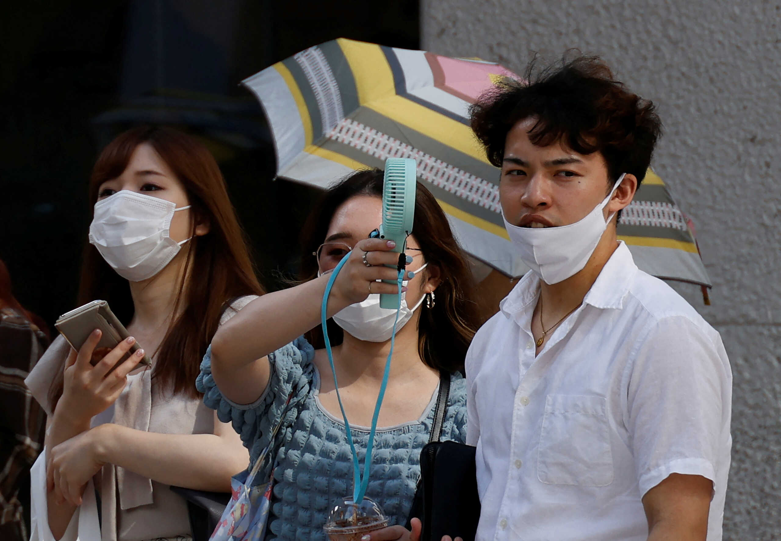 Pedestrians uses a portable fan on the street during a heatwave in Tokyo, Japan, June 27, 2022. REUTERS