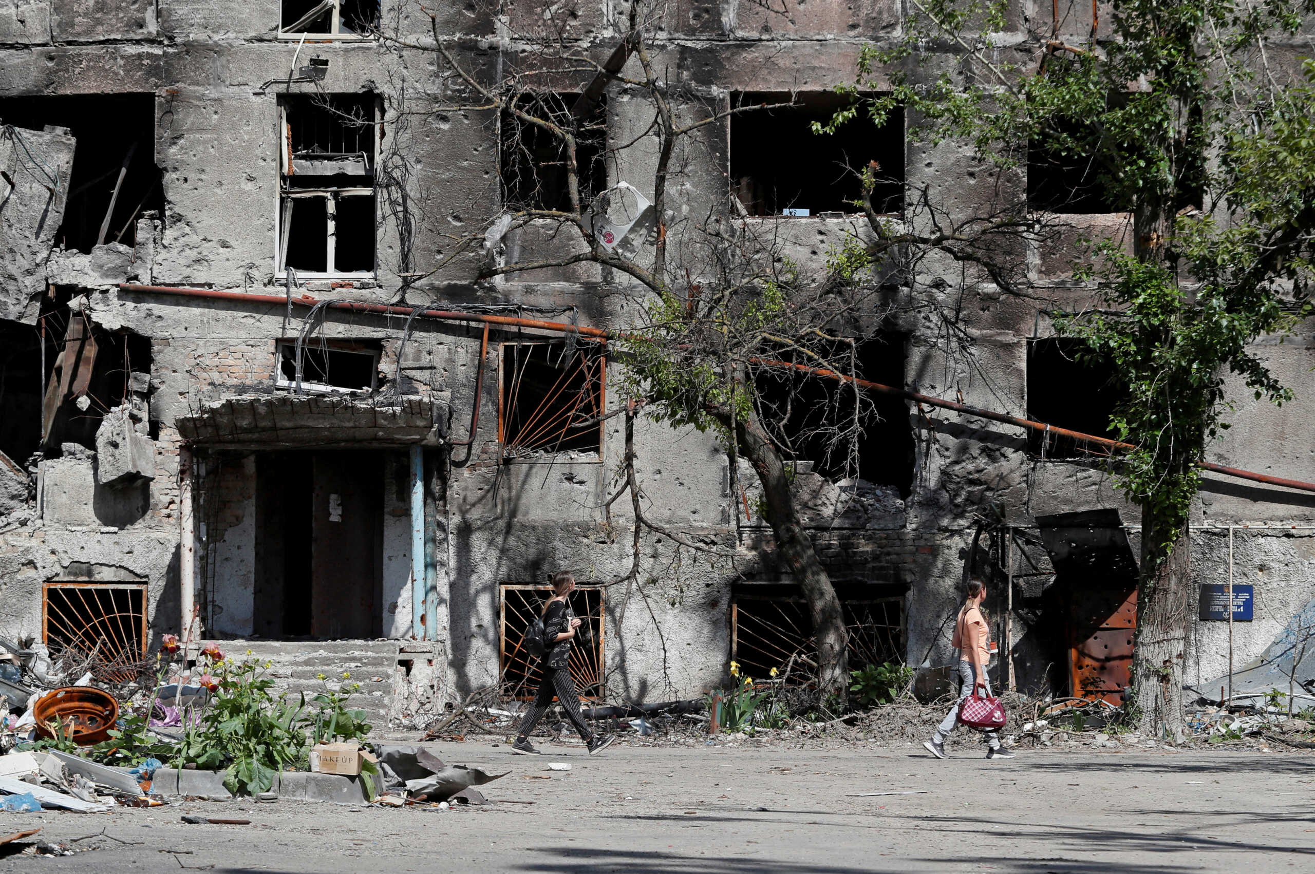 FILE PHOTO: People walk past a residential building heavily damaged during Ukraine-Russia conflict in the southern port city of Mariupol, Ukraine May 30, 2022. REUTERS