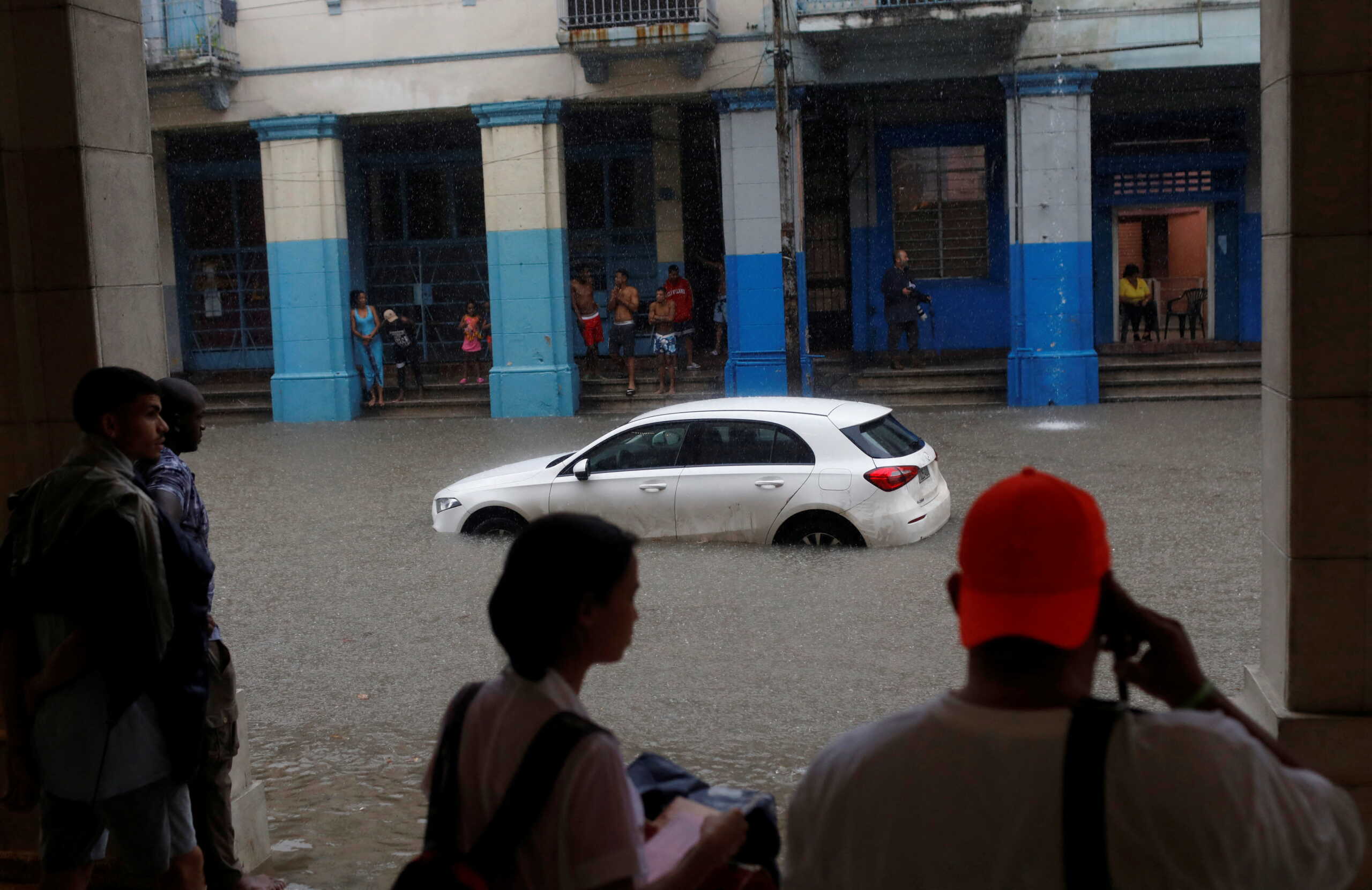 People cover themselves from heavy rain next to a broken-down car in Havana, Cuba, June 3, 2022. REUTERS