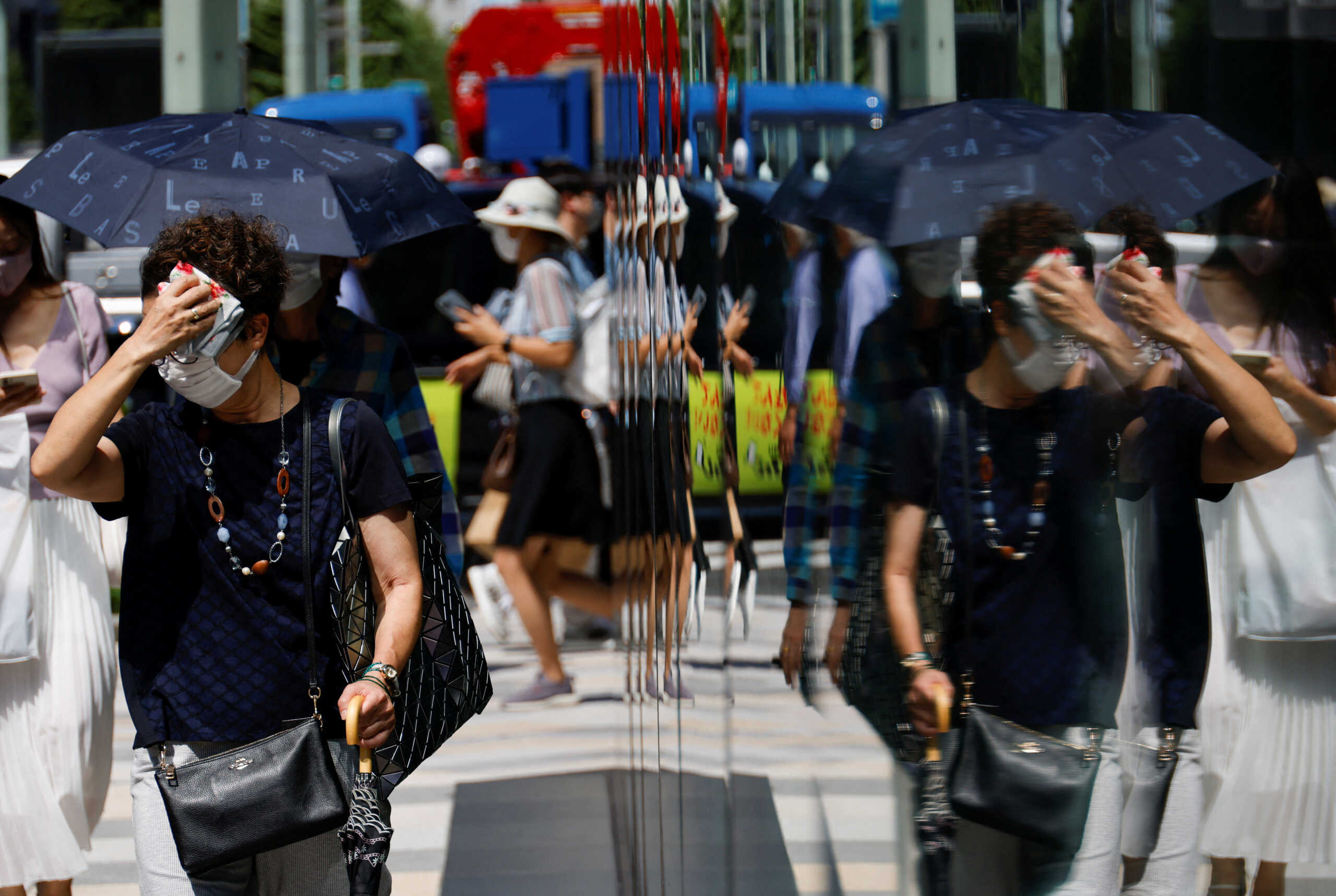 A woman wiping her face is reflected on a window while she walks on a street, as the Japanese government issues a warning over a possible power crunch due to a heatwave in Tokyo, Japan June 28, 2022.  REUTERS