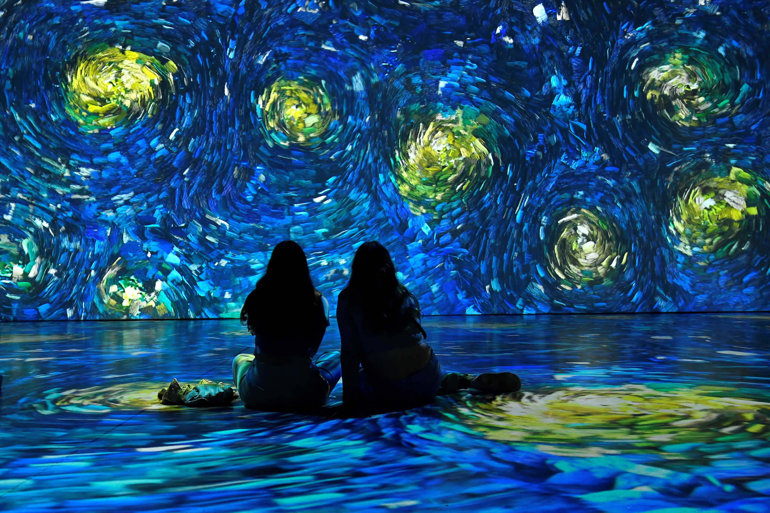 Friends sit on the ground during a Van Gogh 'Immersive Journey' projection, in Dublin, Ireland, June 23, 2022. REUTERS