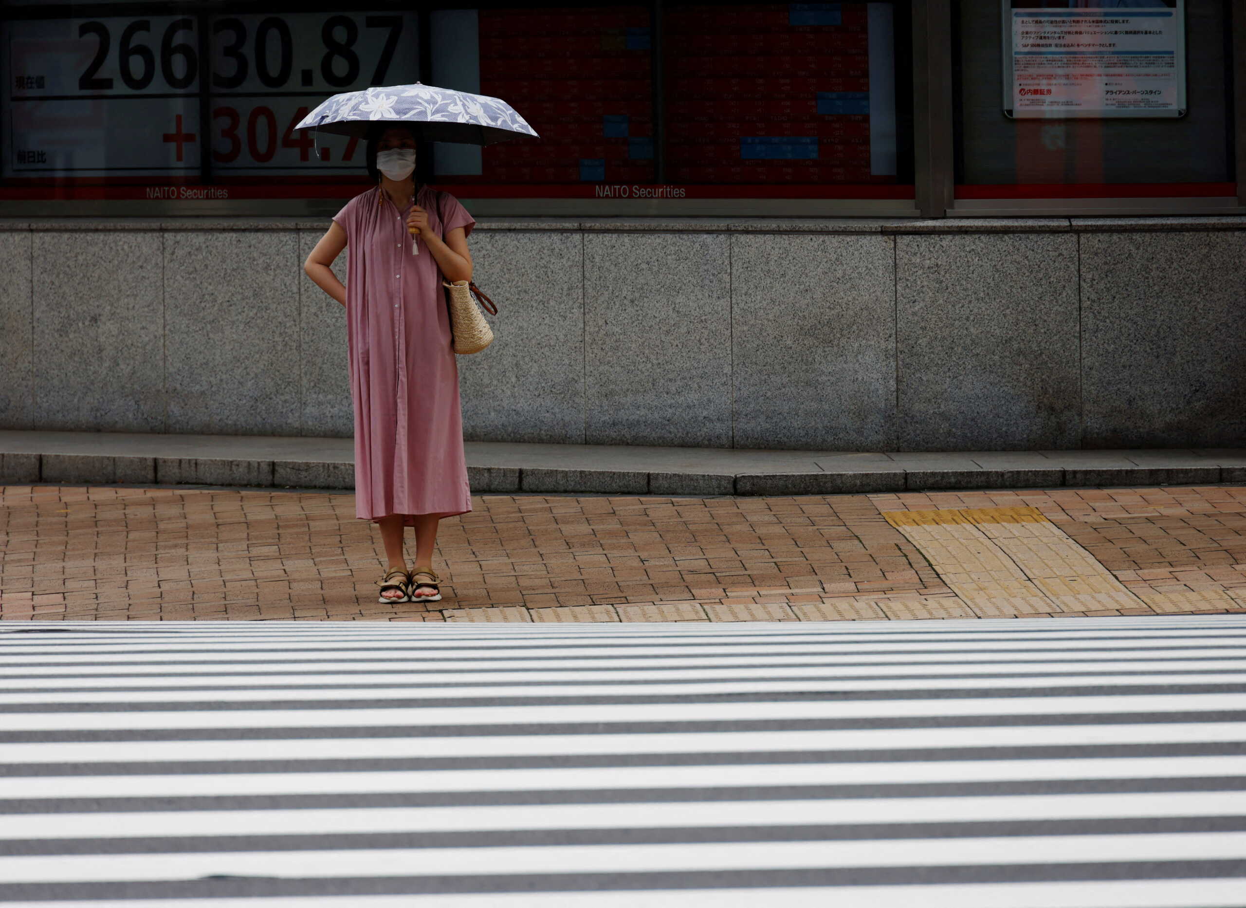 A woman wearing a protective mask amid the coronavirus disease (COVID-19) outbreak, stands in front of an electronic board displaying Japan's Nikkei index outside a brokerage in Tokyo, Japan June 16, 2022. REUTERS