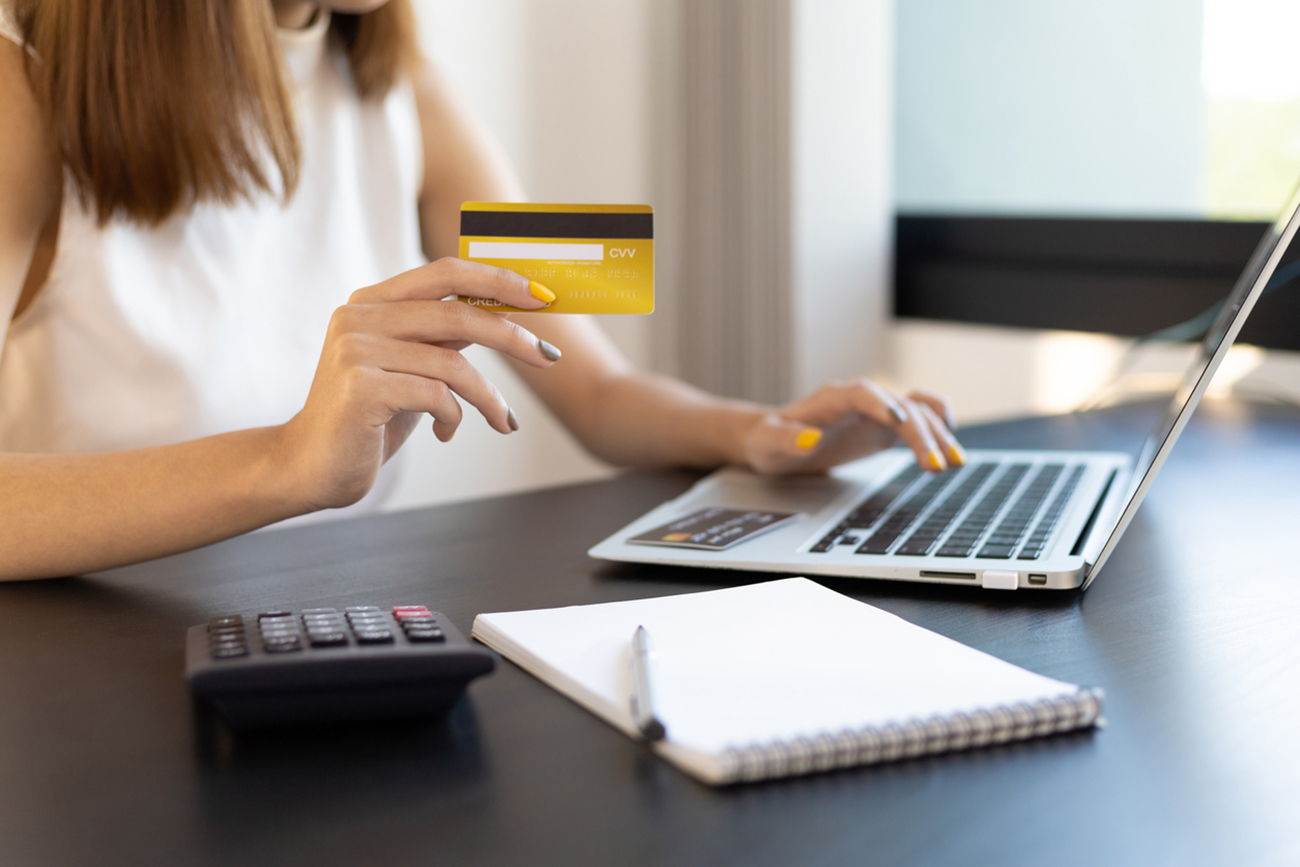 Woman holding credit card using laptop at home and shopping online. Financial planning ideas and expenses.