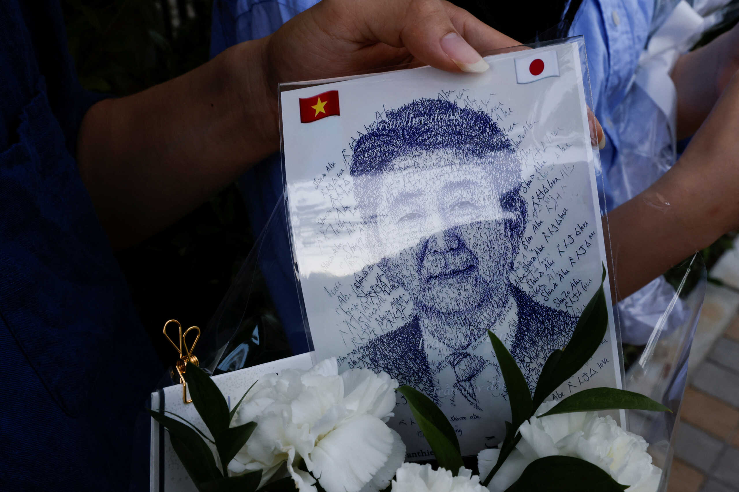 Kieu Van Thiet and Hoang Thi Phuong, Vietnamese living in Japan, show an image of former Japanese Prime Minister Shinzo Abe as they mourn outside his residence in Tokyo, Japan July 10, 2022. REUTERS