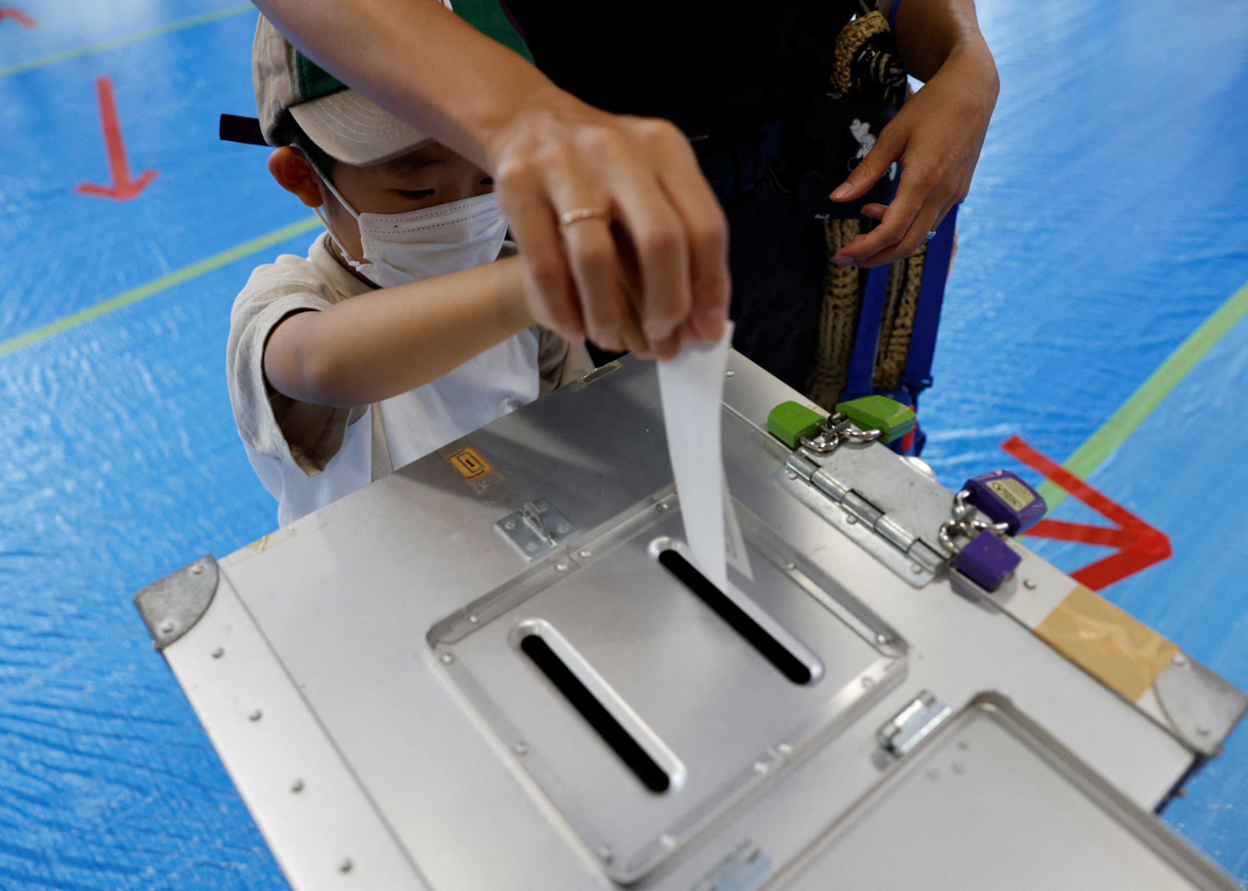 Asamori Ishii (6) tries to cast his mother's ballot with her help during the upper house election at a polling station in Tokyo, Japan July 10, 2022. REUTERS
