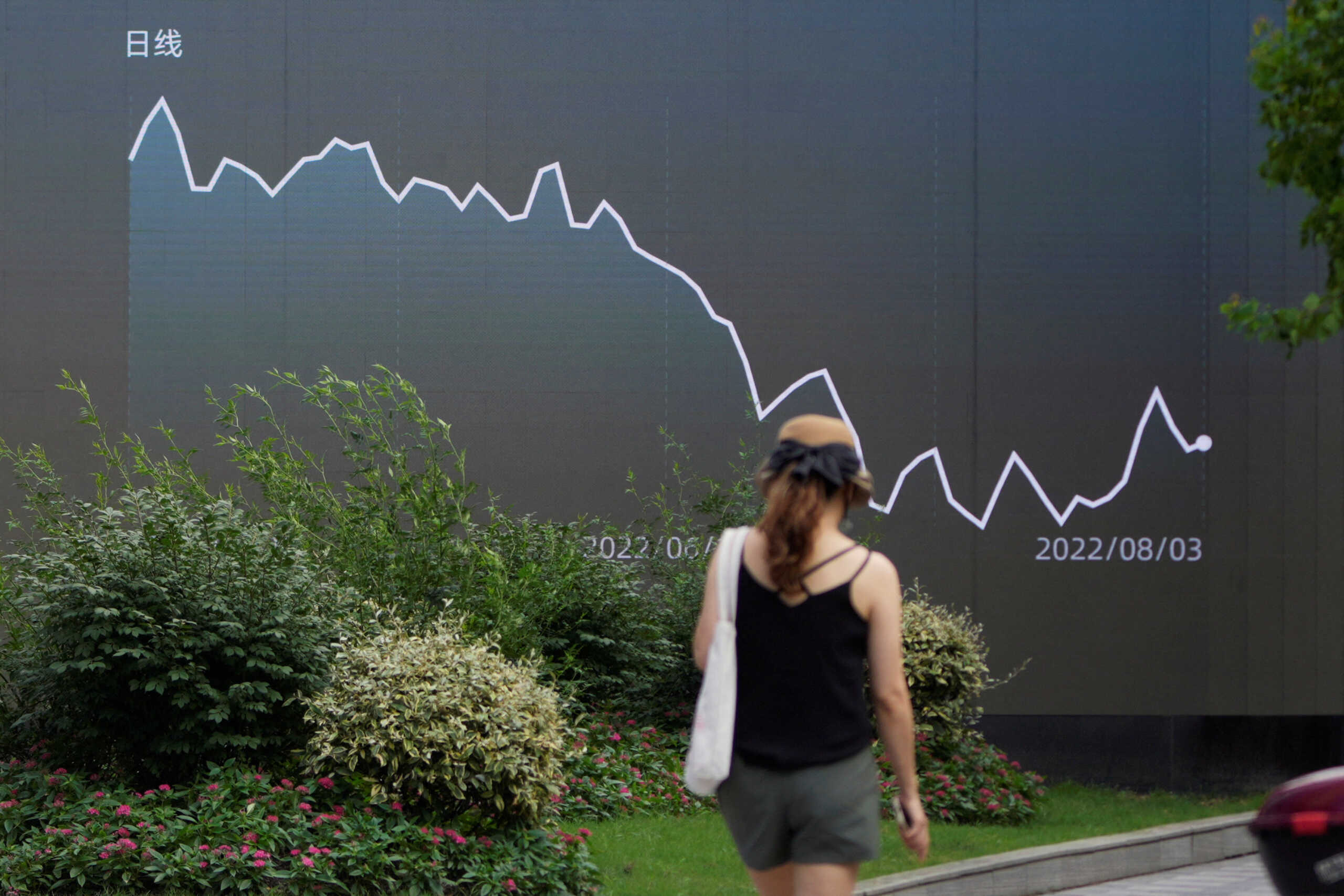 A pedestrian walks past a giant display showing a stock graph, in Shanghai, China August 3, 2022. REUTERS