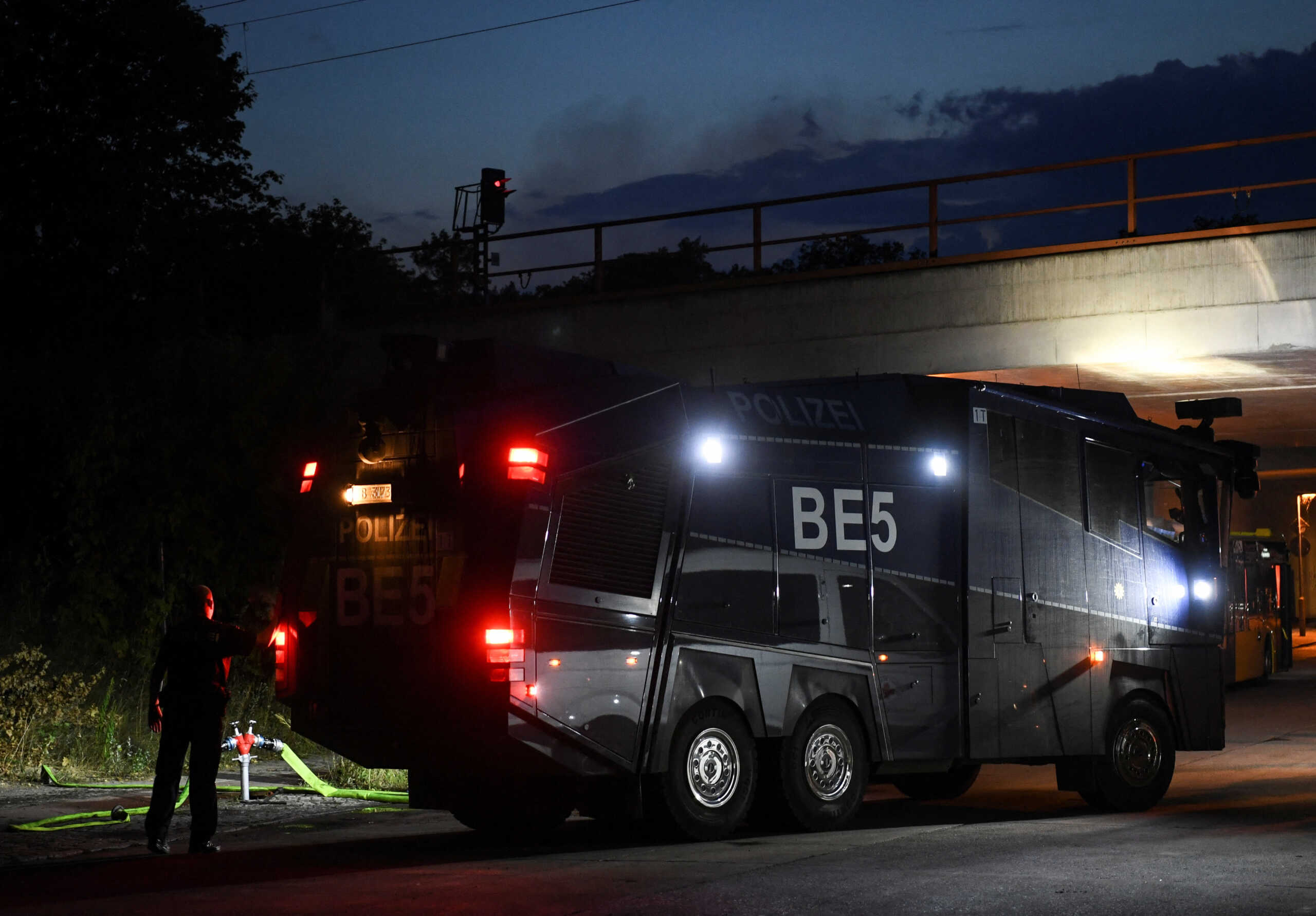 A police water cannon vehicle is seen near the closed motorway access Huettenweg, as smoke rises in the background, due to an explosion in munitions depot in the Grunewald forest in Berlin, Germany August 4, 2022. REUTERS