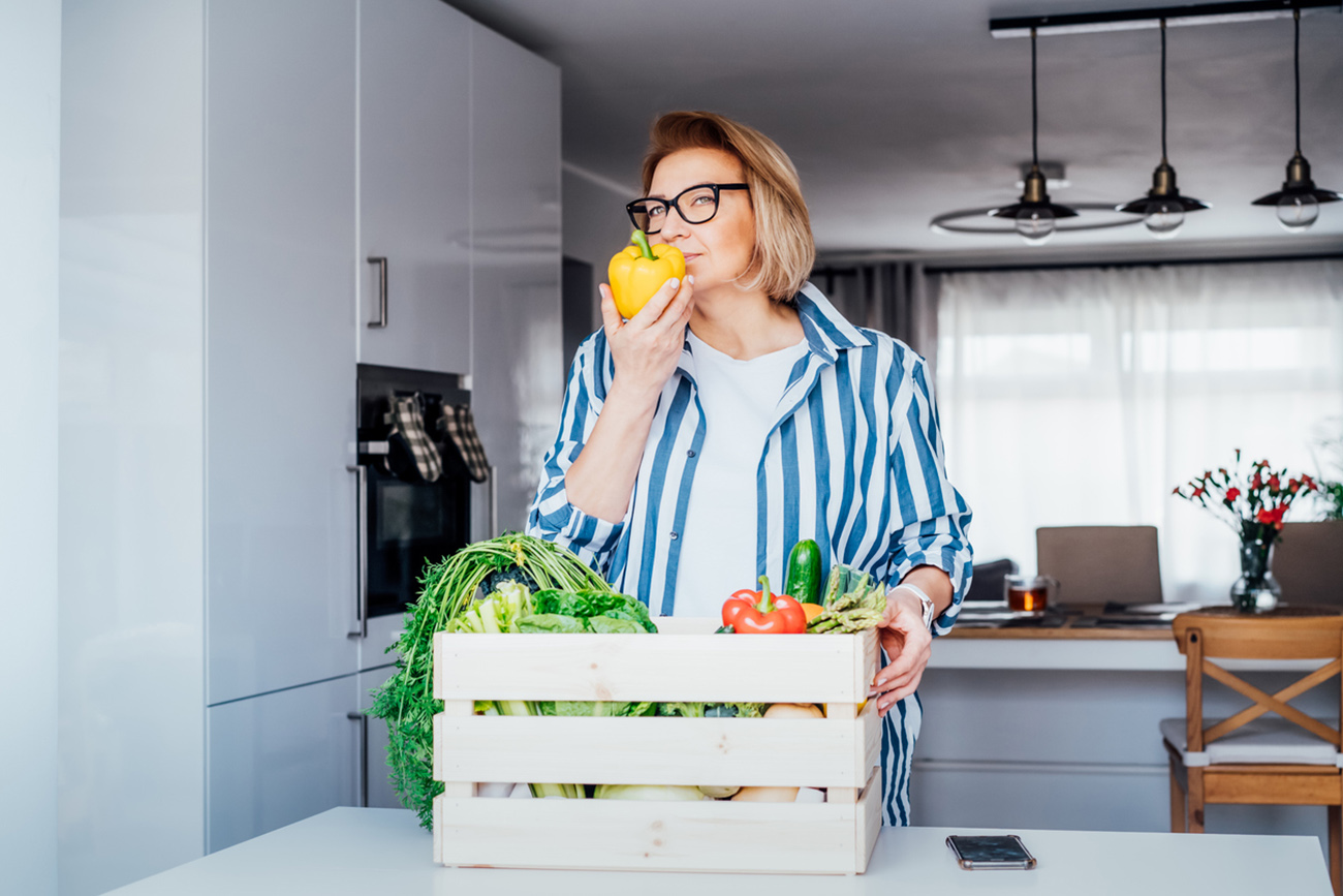 Woman checking fresh organic bell pepper from a wooden box with fresh vegetables. Local farmer healthy food. New Start of a healthy life, weight loss concept. Online home food delivery. Copy space.