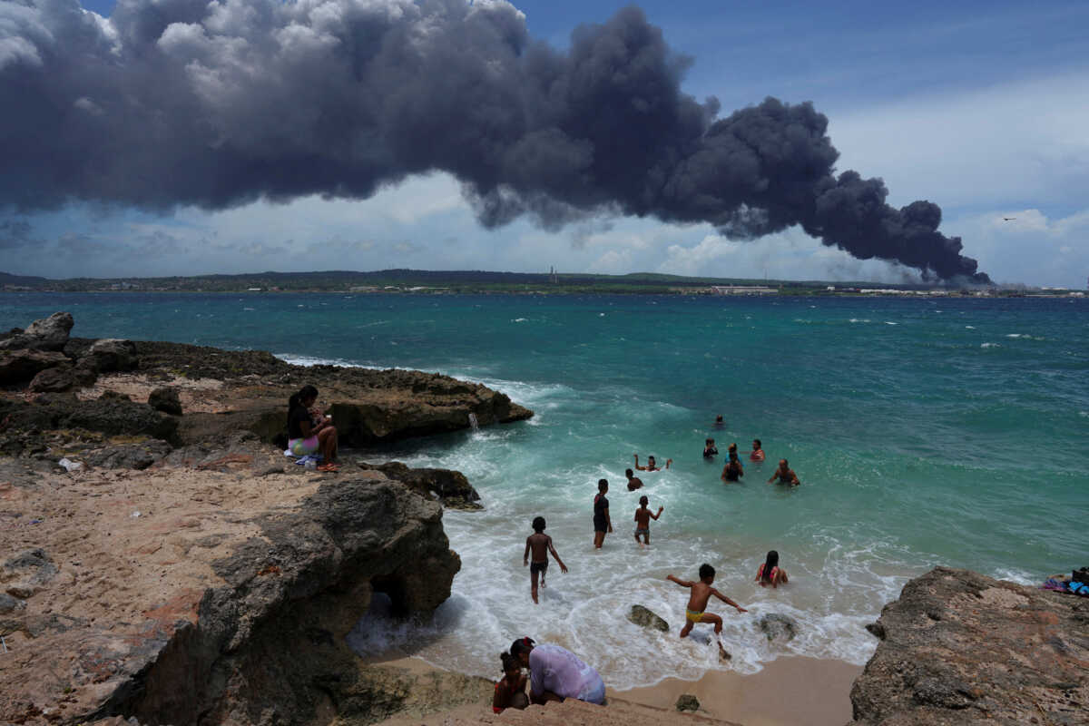 People enjoy the beach near the smoke of a fire over fuel storage tanks that exploded near Cuba's supertanker port in Matanzas, Cuba, August 6, 2022. REUTERS