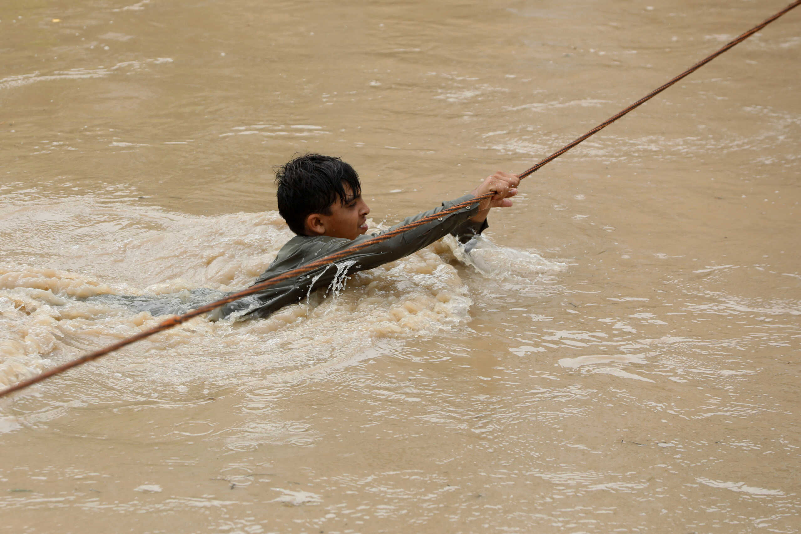 A boy crosses a flooded street, with the help of a wire fastened on both ends, following rains and floods during the monsoon season in Charsadda, Pakistan August 27, 2022. REUTERS