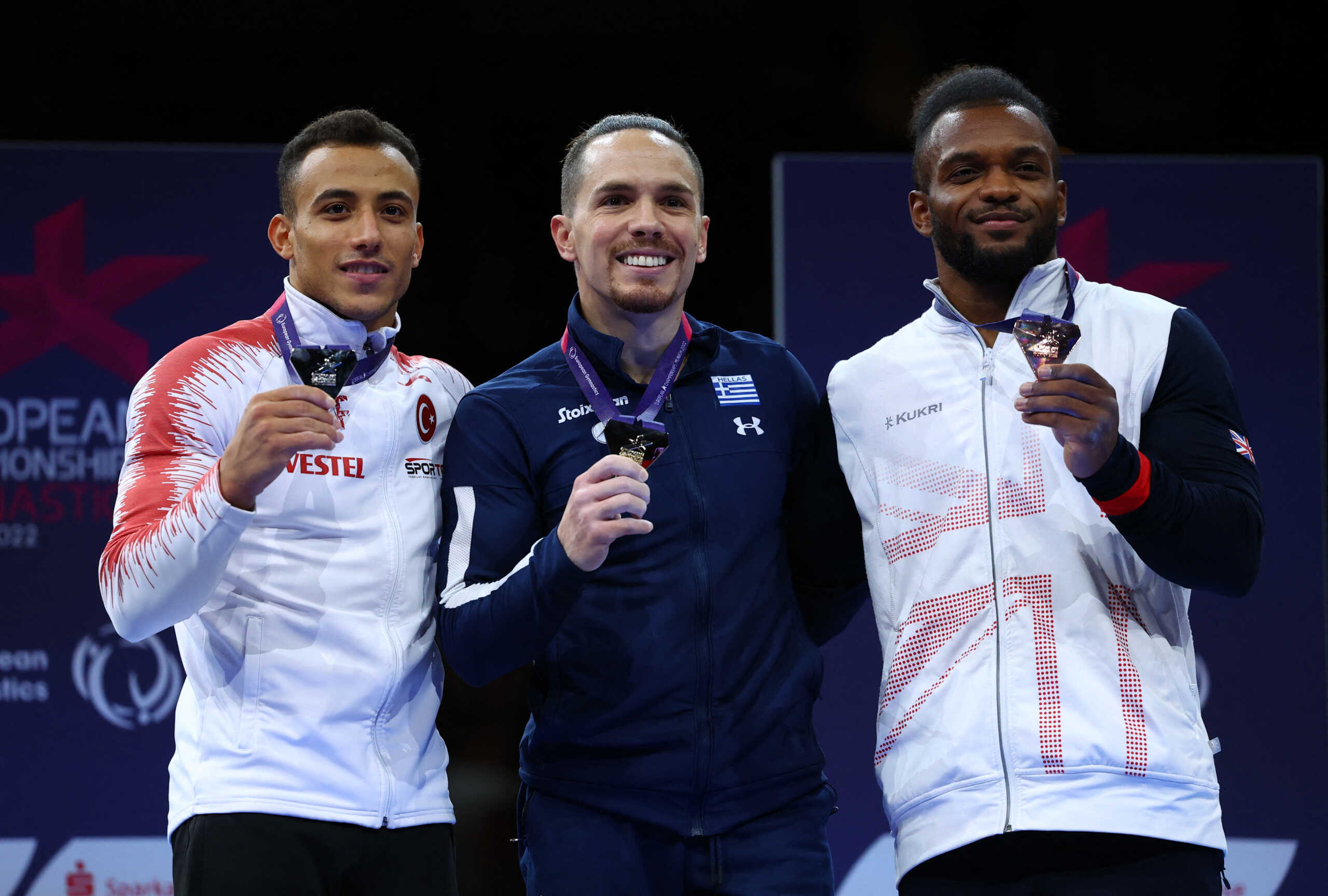 2022 European Championships - Artistic Gymnastics - Olympiahalle, Munich, Germany - August 21, 2022 Gold medallist Greece's Aleftherios Petrounias celebrates on the podium after winning the Men's Rings Final alongside silver medallist Turkey's Adem Asil and bronze medallist Britain's Courtney Tulloch REUTERS