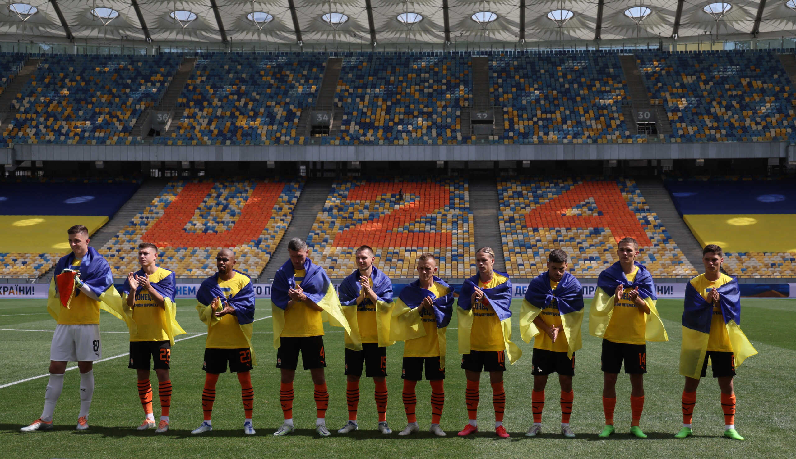 Soccer Football - Ukrainian Premier League - Shakhtar Donetsk v FC Metalist 1925 Kharkiv - NSC Olympiyskiy, Kyiv, Ukraine - August 23, 2022 Shakhtar Donetsk players draped with Ukrainian flags applaud as they line up before the match as Russia's attack on Ukraine continues REUTERS