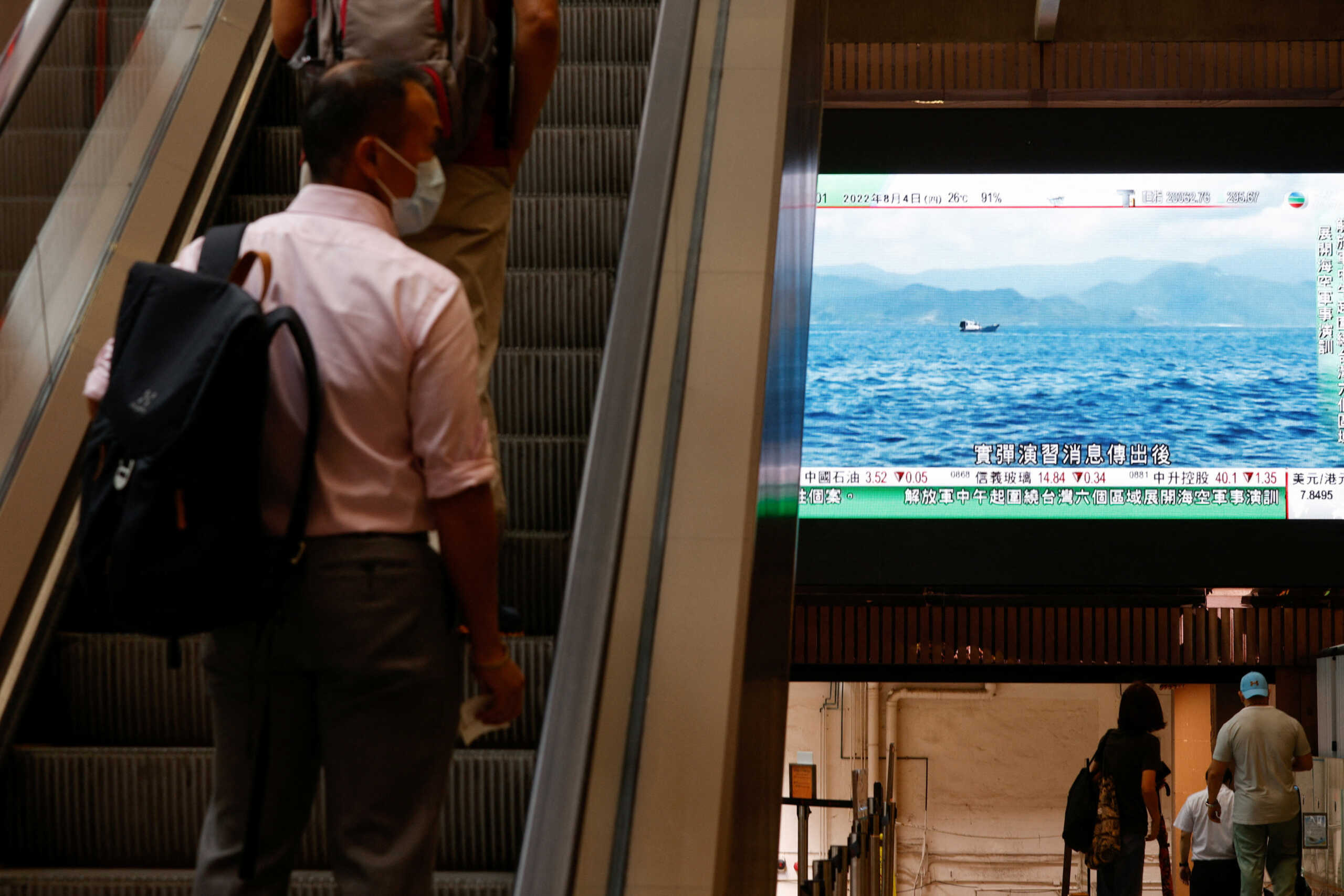 A man rides an elevator as a TV screen shows that China's People's Liberation Army has begun military exercises including live firing on the waters and in the airspace surrounding the island of Taiwan, as reported by Chinese state television, in Hong Kong, China August 4, 2022. REUTERS