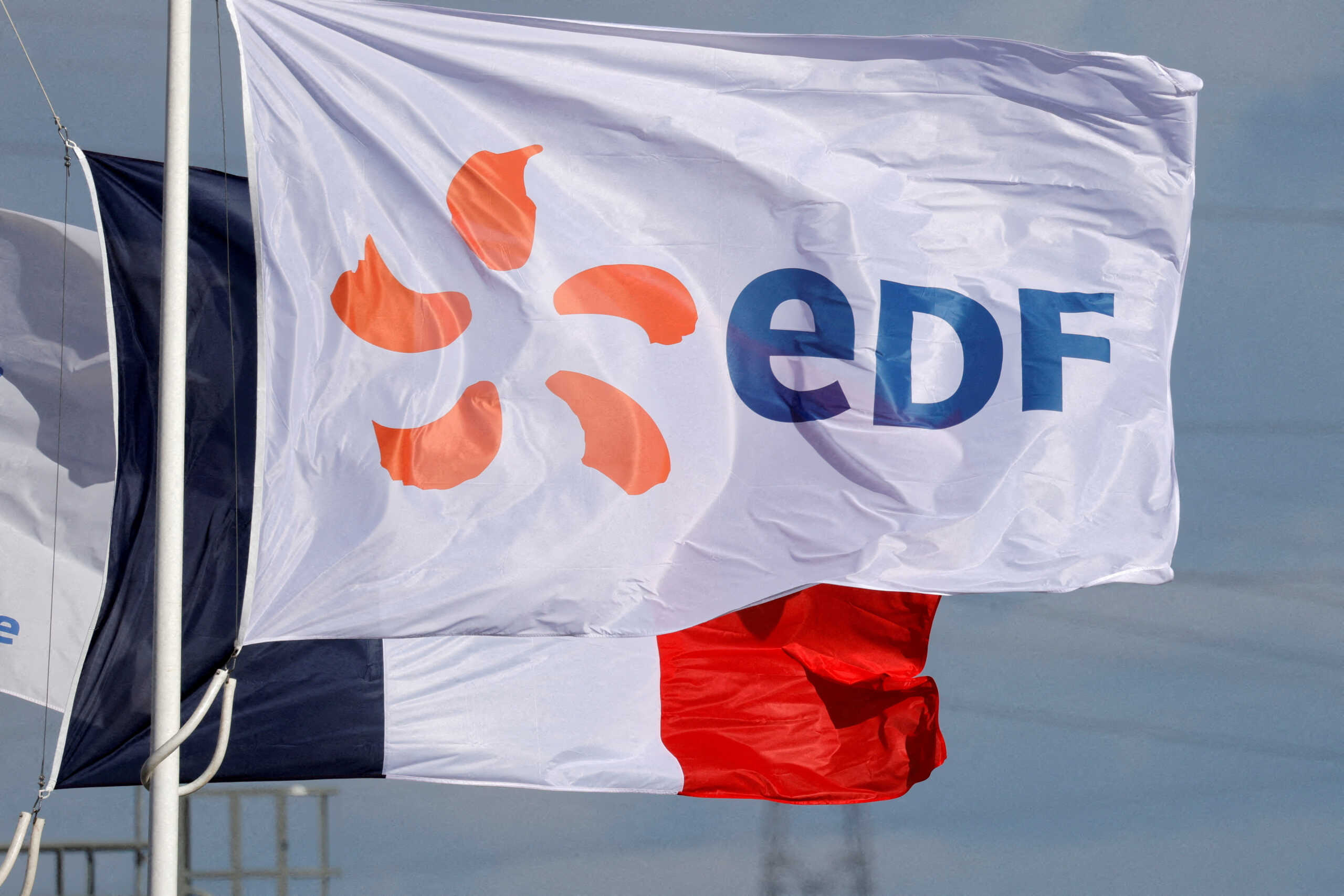 FILE PHOTO: A flag with the company logo of Electricite de France (EDF) and a French flag fly next to the EDF power plant in Bouchain, near Valenciennes, France, September 29, 2021. REUTERS