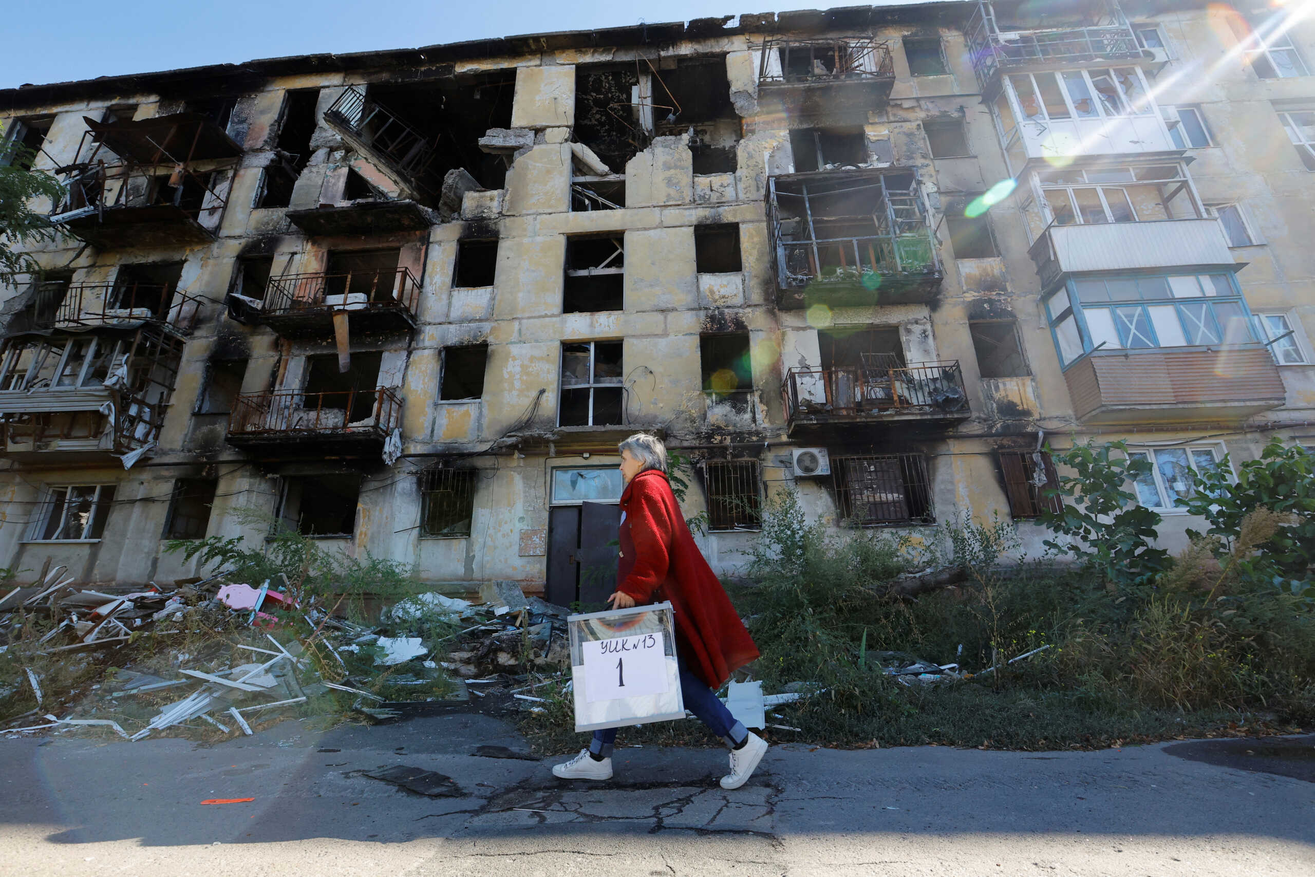 A member of an electoral commission walks past a destroyed building with a mobile ballot box and documents while visiting local residents on the third day of a referendum on the joining of the self-proclaimed Donetsk People's Republic (DPR) to Russia, in Mariupol, Ukraine September 25, 2022. REUTERS