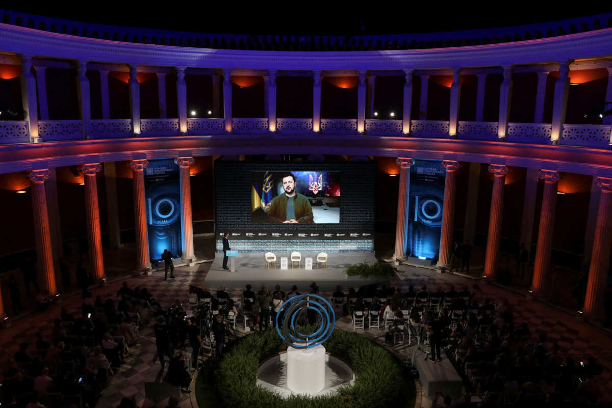 People watch as Ukrainian President Volodymyr Zelenskiy is seen on the screen as he speaks, during the Athens Democracy Forum, at the Zappeion Hall in Athens, Greece, September 28, 2022. REUTERS