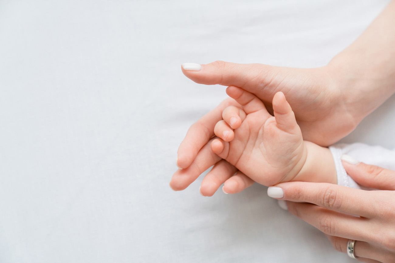 Close up image of a mother`s mom hand holding her little small toddler`s infant newborn tiny hand on white background. Childcare, motherhood concept.