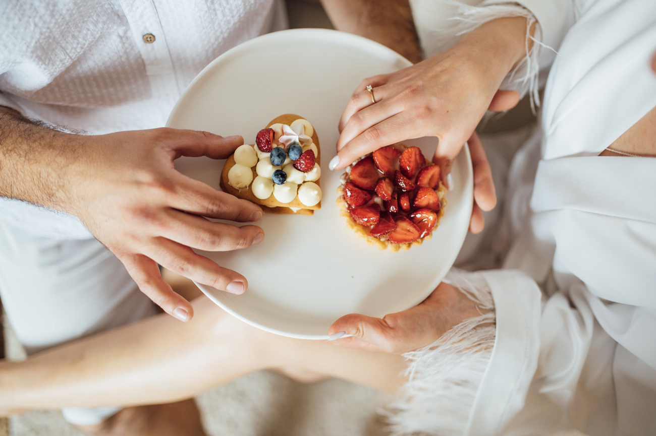 happy couple having breakfast in bed with delicious cookies with strawberries on top.