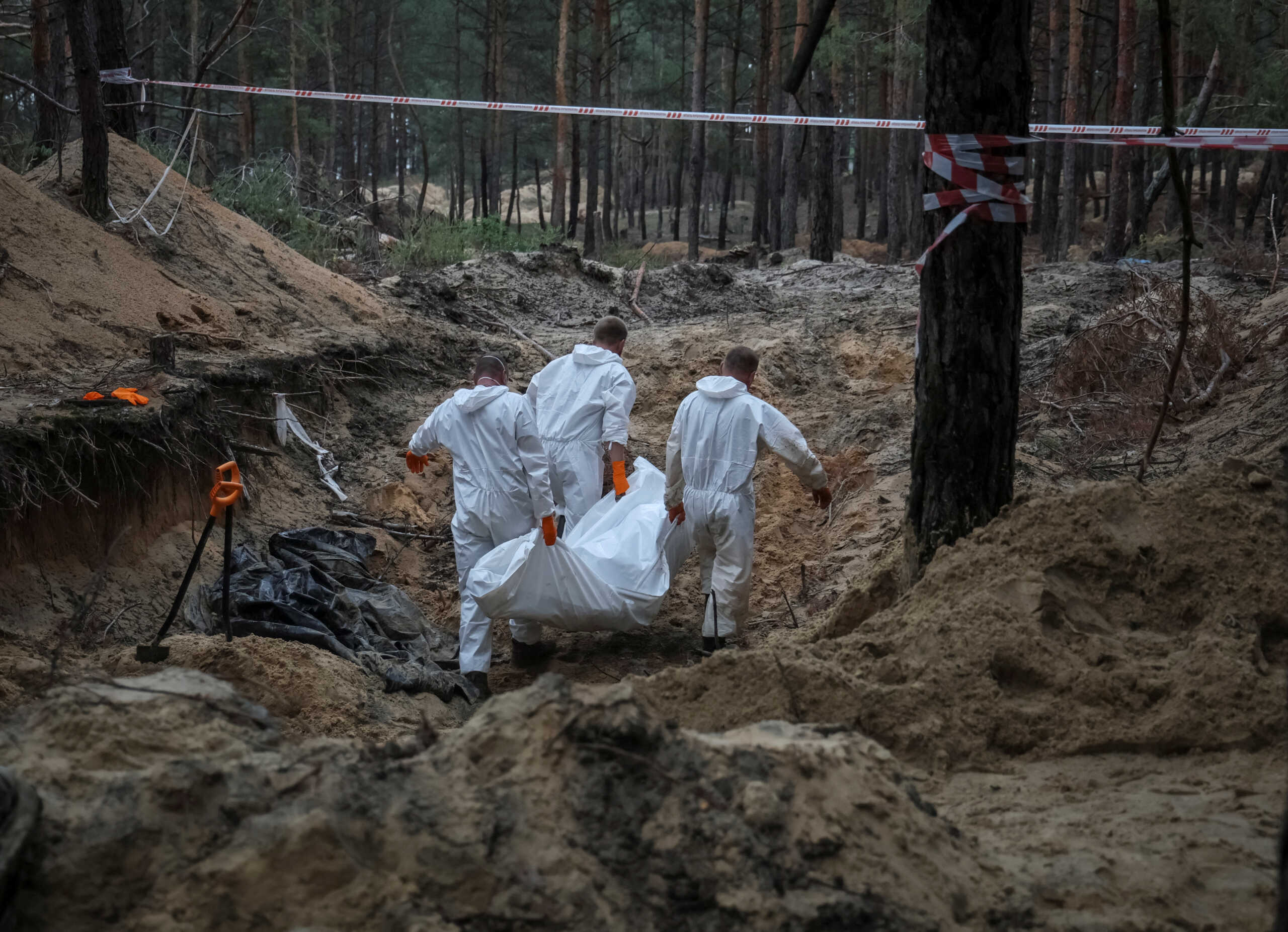 Experts carry a body as they work at a place of mass burial during an exhumation, as Russia's attack on Ukraine continues, in the town of Izium, recently liberated by Ukrainian Armed Forces, in Kharkiv region, Ukraine September 16, 2022.  REUTERS