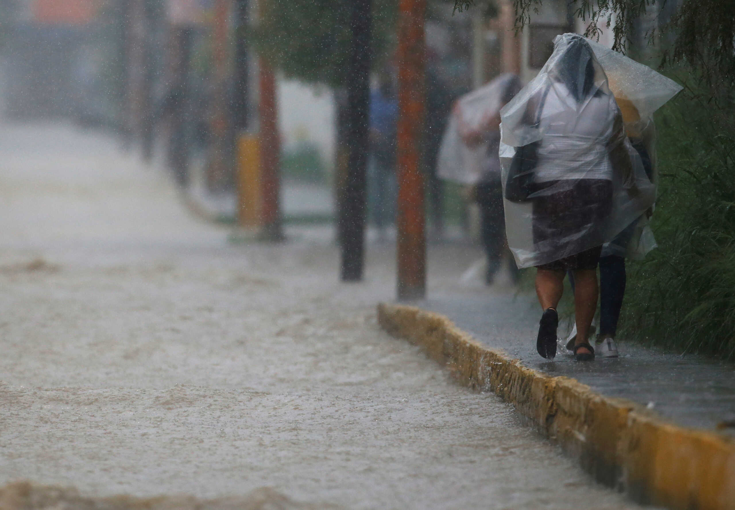 People covered with plastic sheeting walk along the sidewalk of a flooded street as heavy rains continue, in Juarez, Mexico September 5, 2022. REUTERS